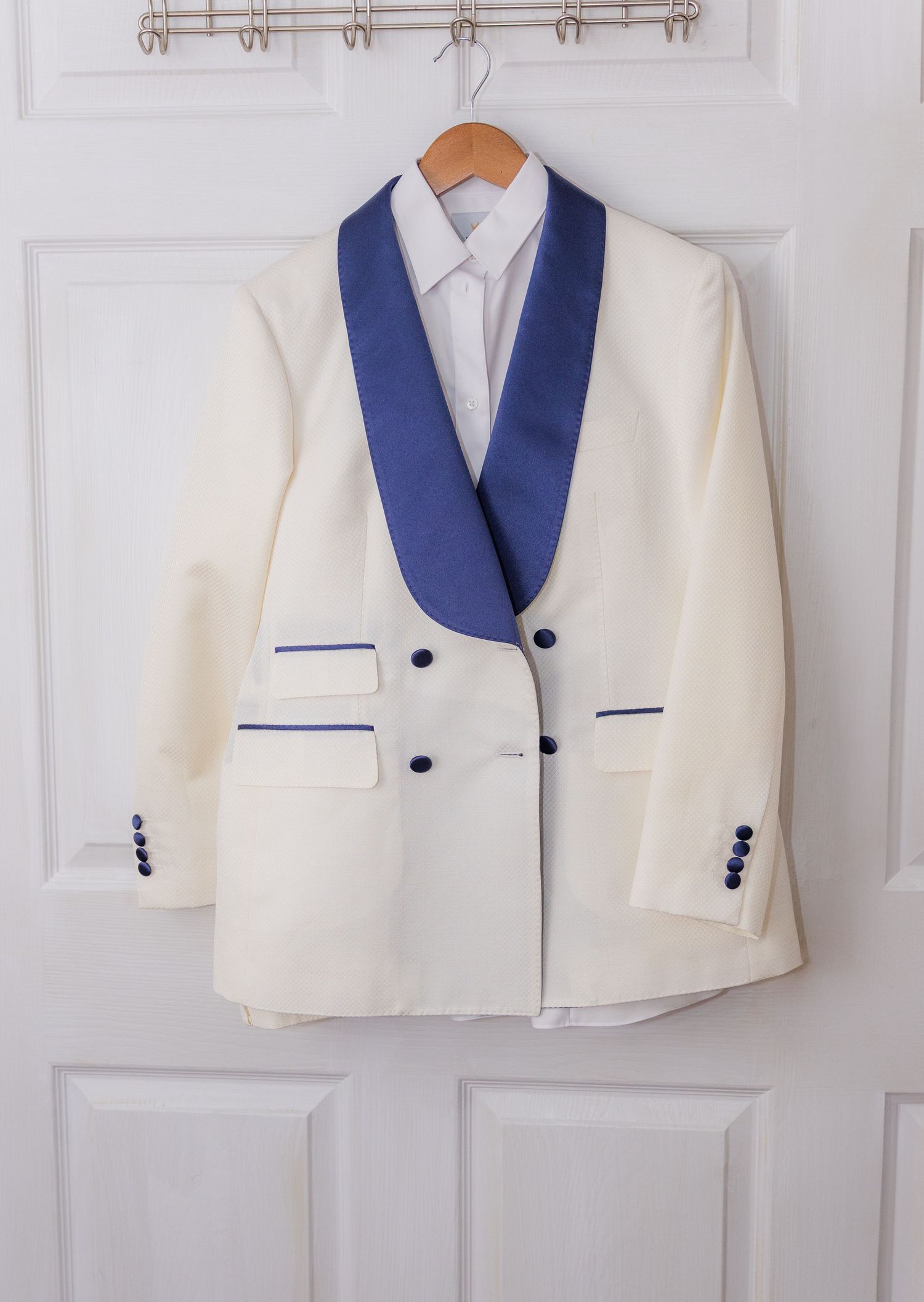 White and navy blue formal suits hanging in a row on wall-mounted rack.