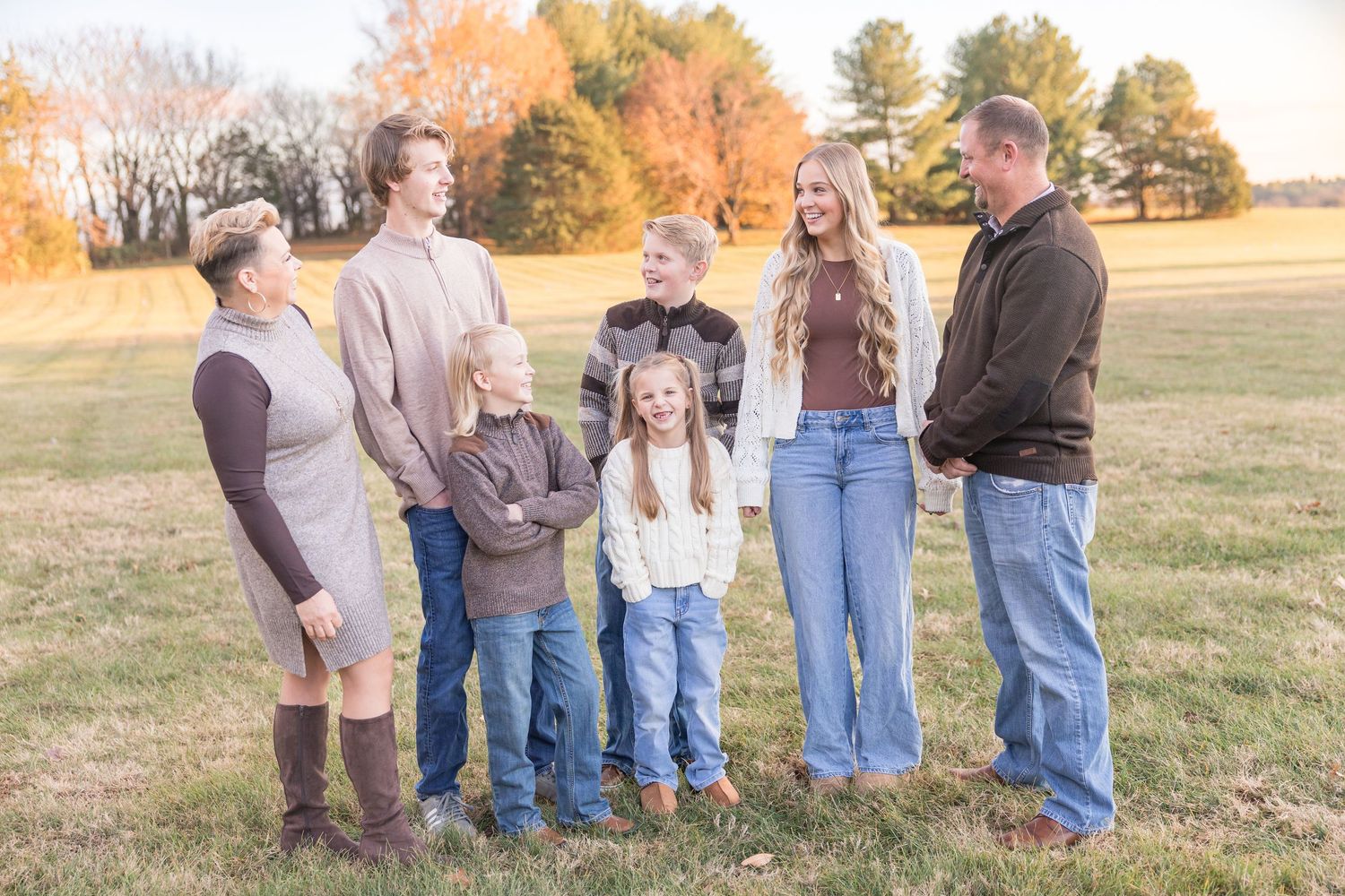 A group of people stand together in a field during autumn with warm golden light and trees in the background.