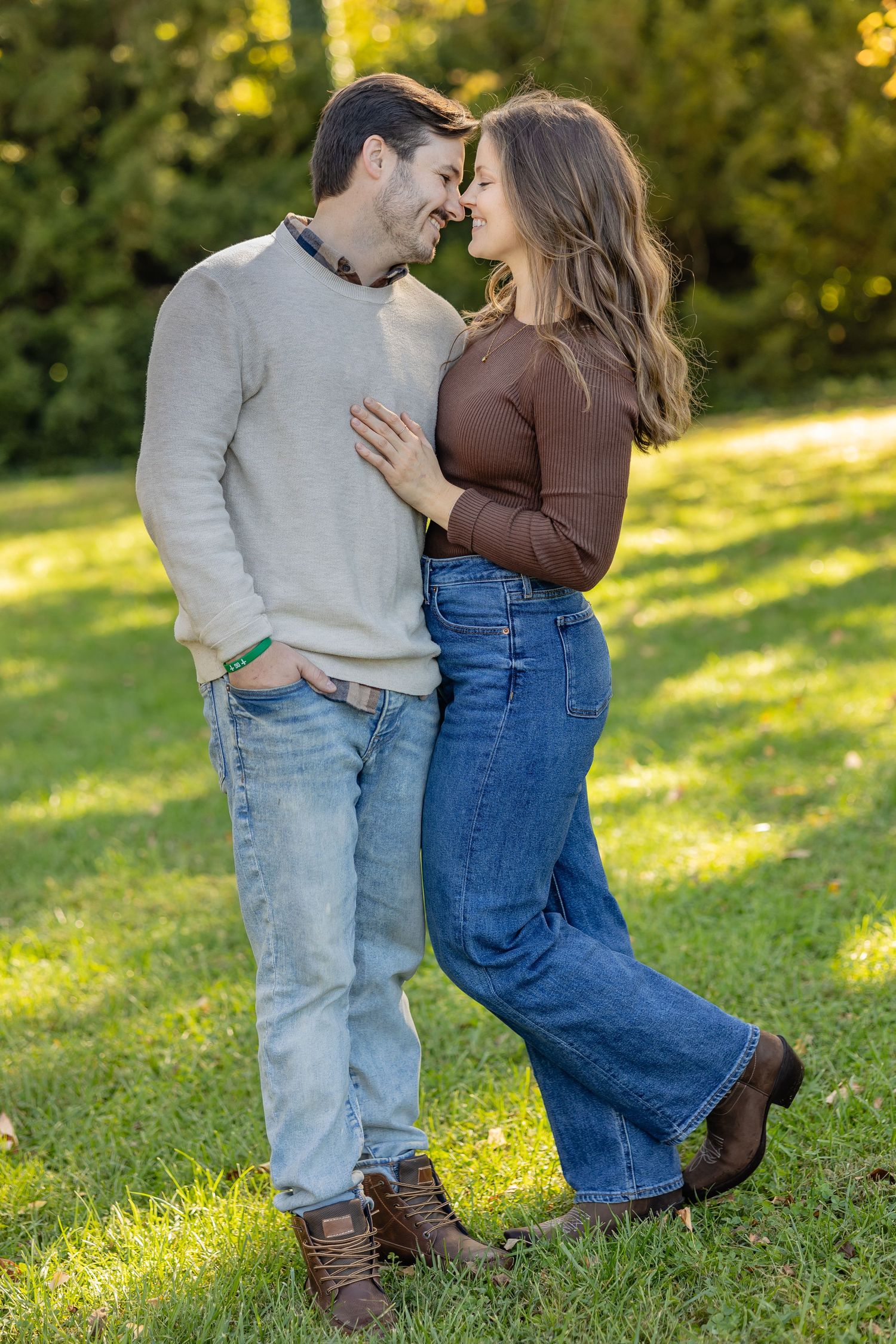 Romantic couple in casual wear embracing on sunny grass during autumn photoshoot.