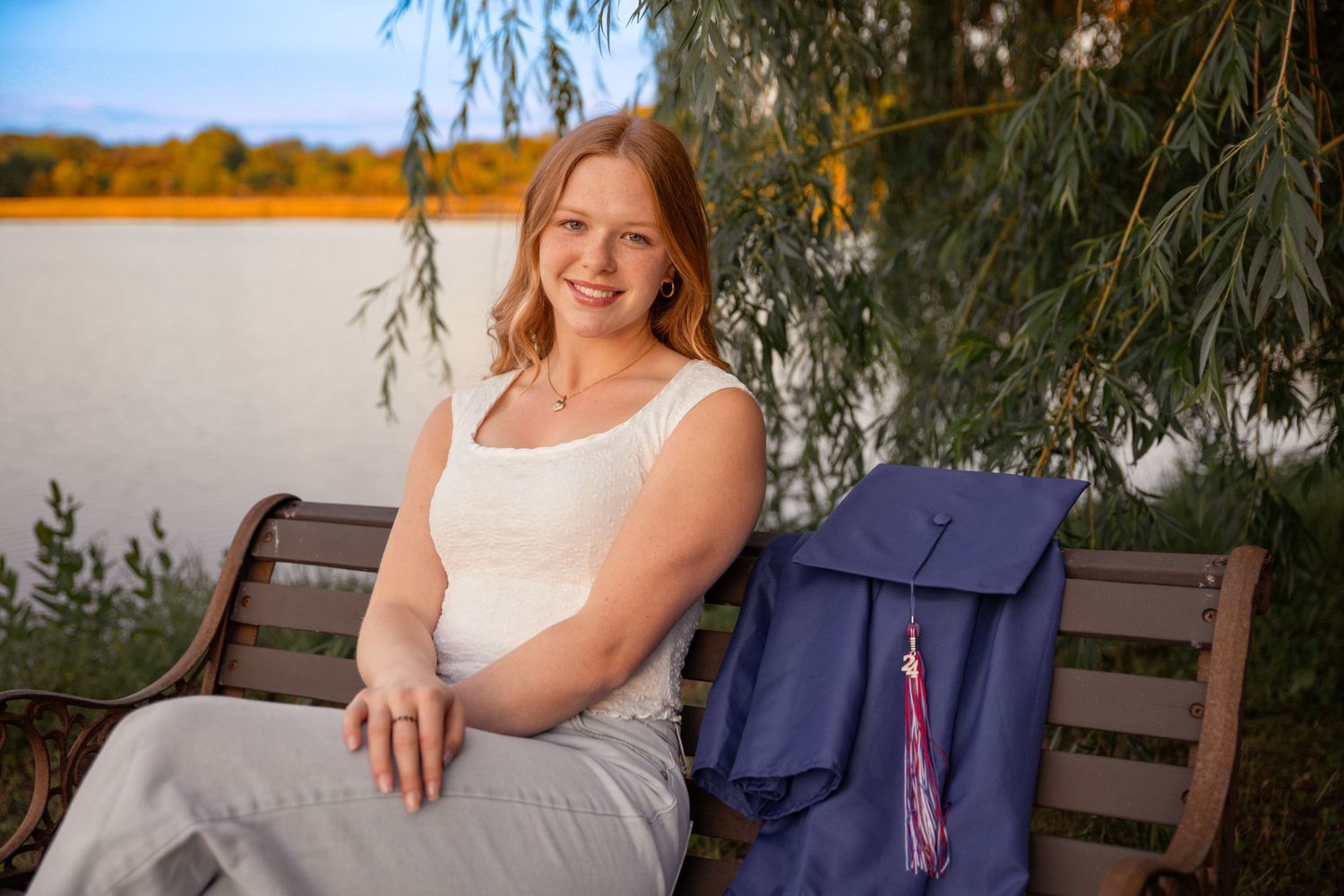 Student relaxing on park bench by lake with backpack.