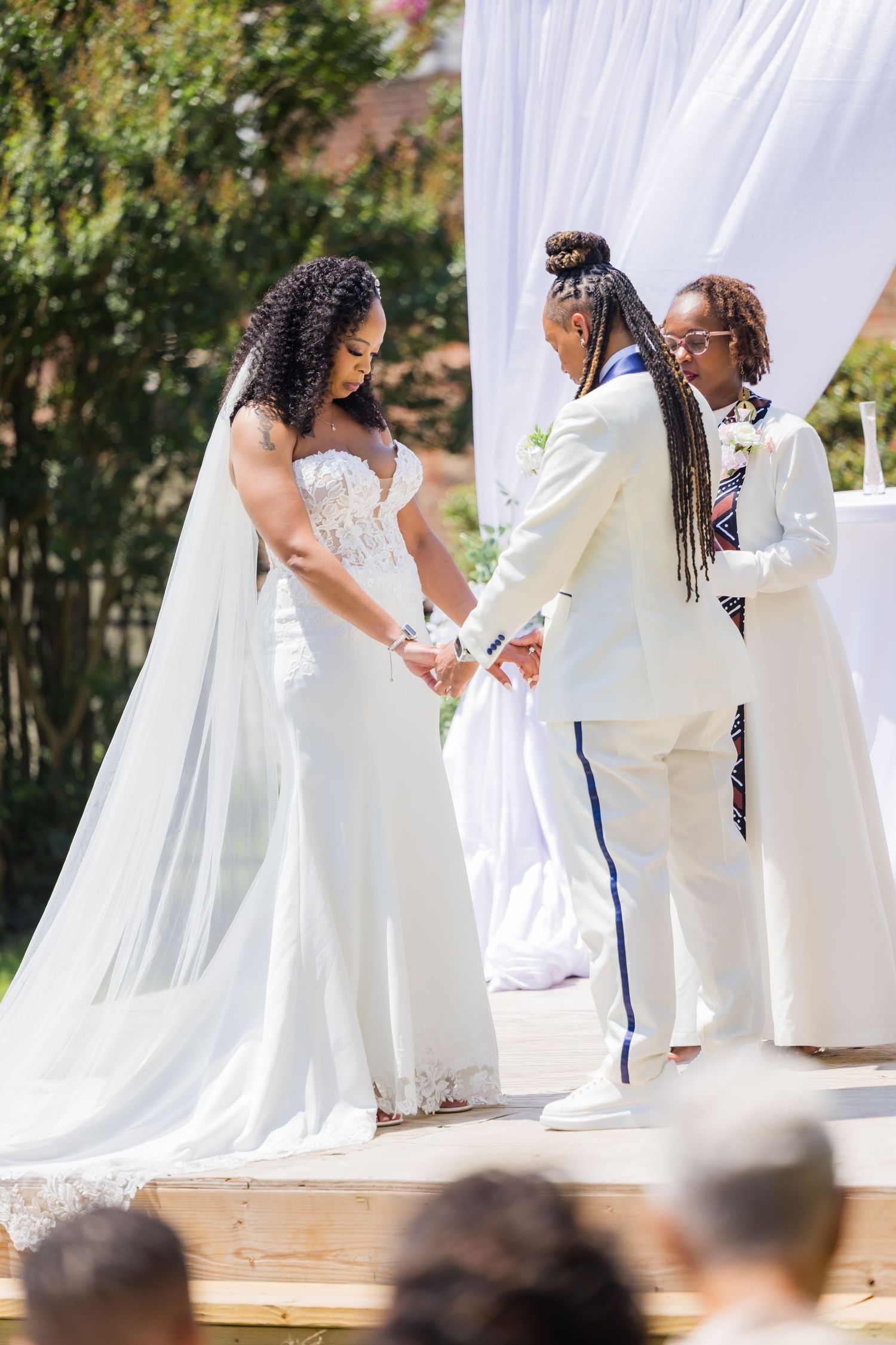 Outdoor wedding ceremony on wooden platform with white draping and floral decorations.