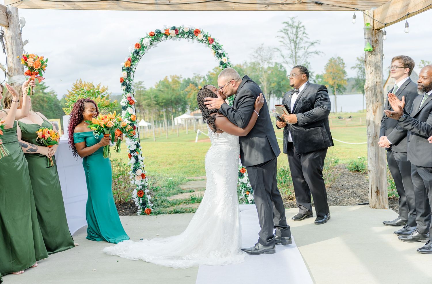 Wedding ceremony moment with bridesmaids in green dresses watching the couple's first kiss.