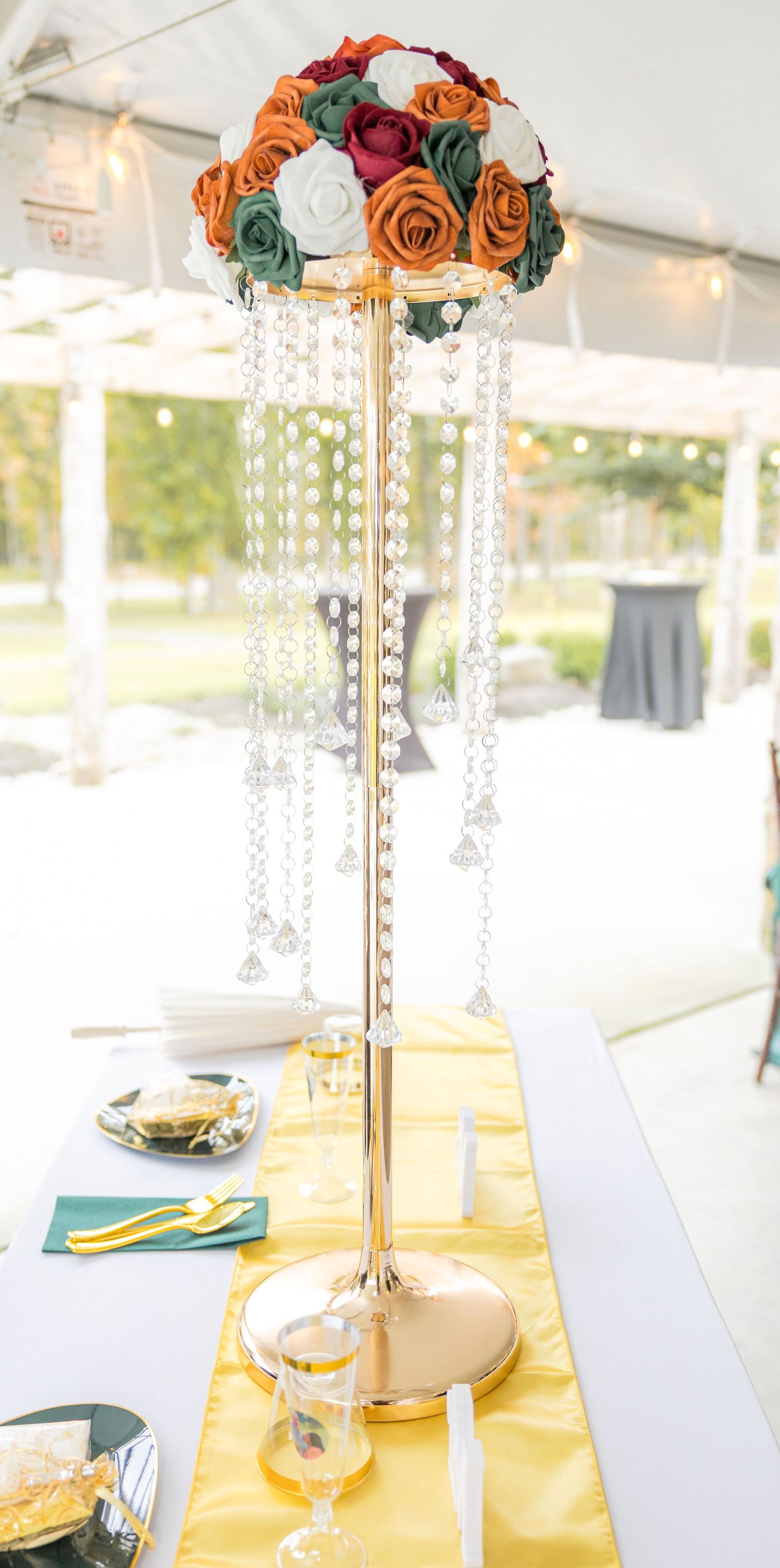 Elegant table centerpieces with orange and burgundy roses on gold stands with crystal accents.
