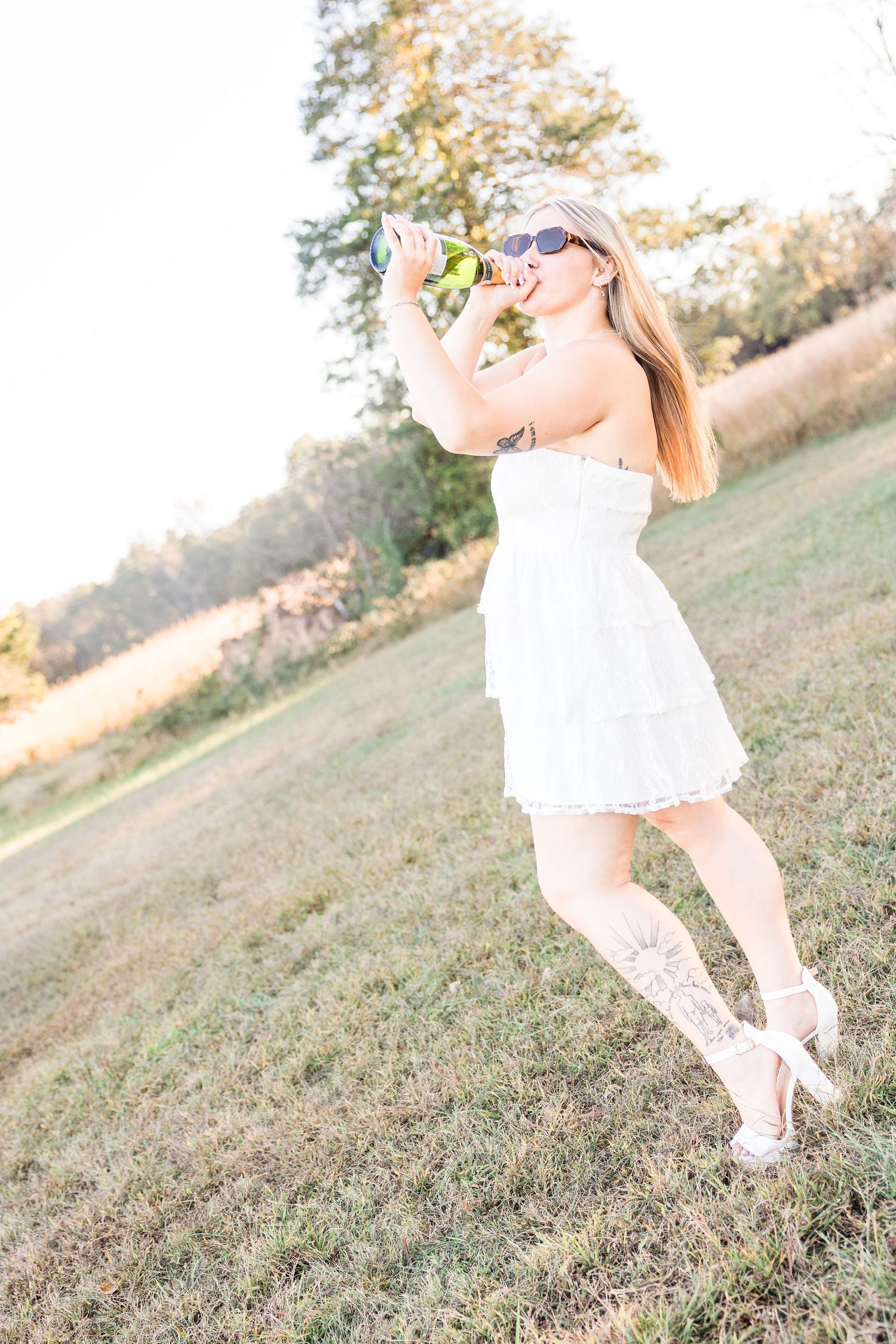 Person in flowing white dress twirls playfully on grassy hillside during golden hour.