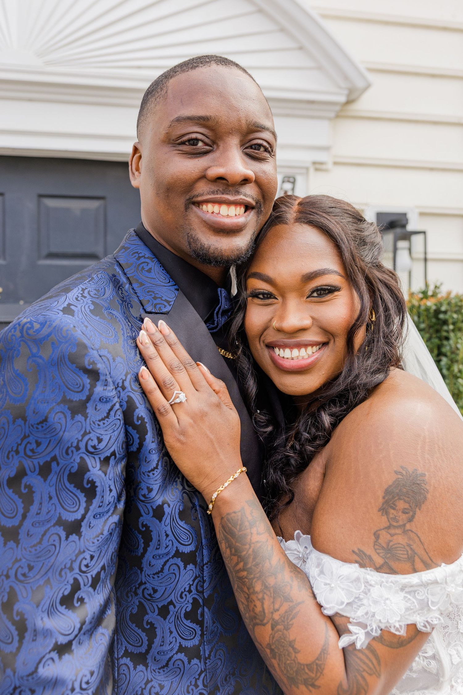 A happy couple embraces in formal wedding attire while showing off an engagement ring.
