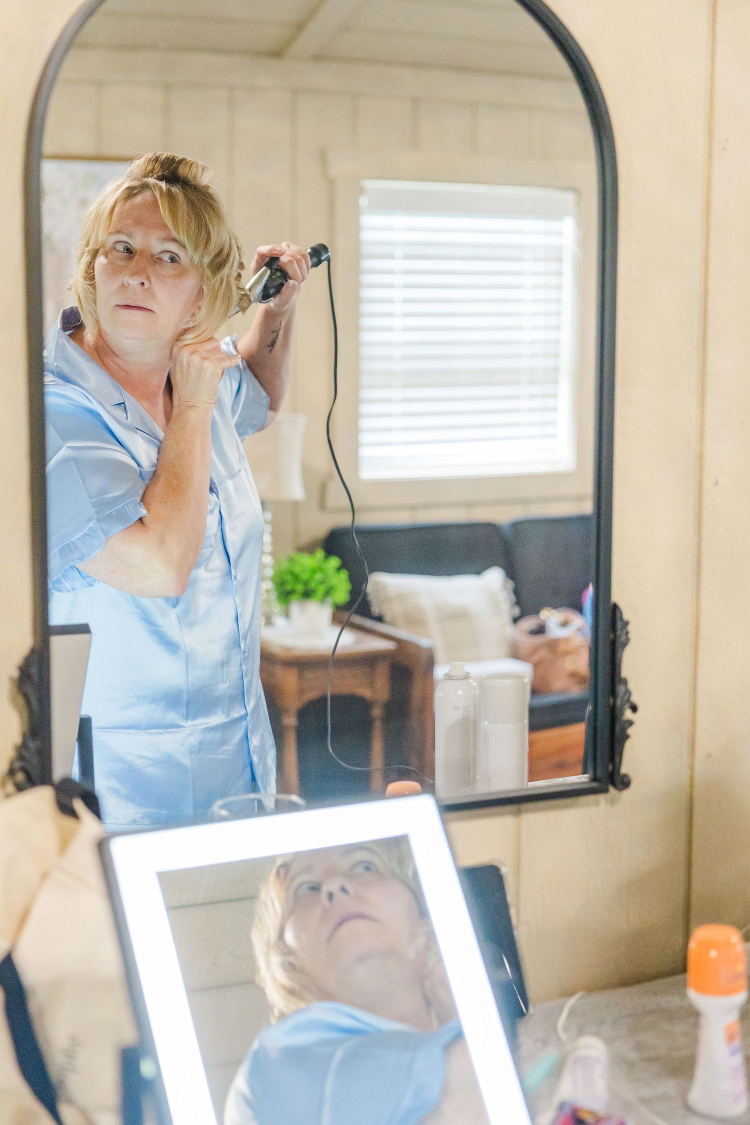 Someone getting ready in front of a mirror wearing a light blue outfit.