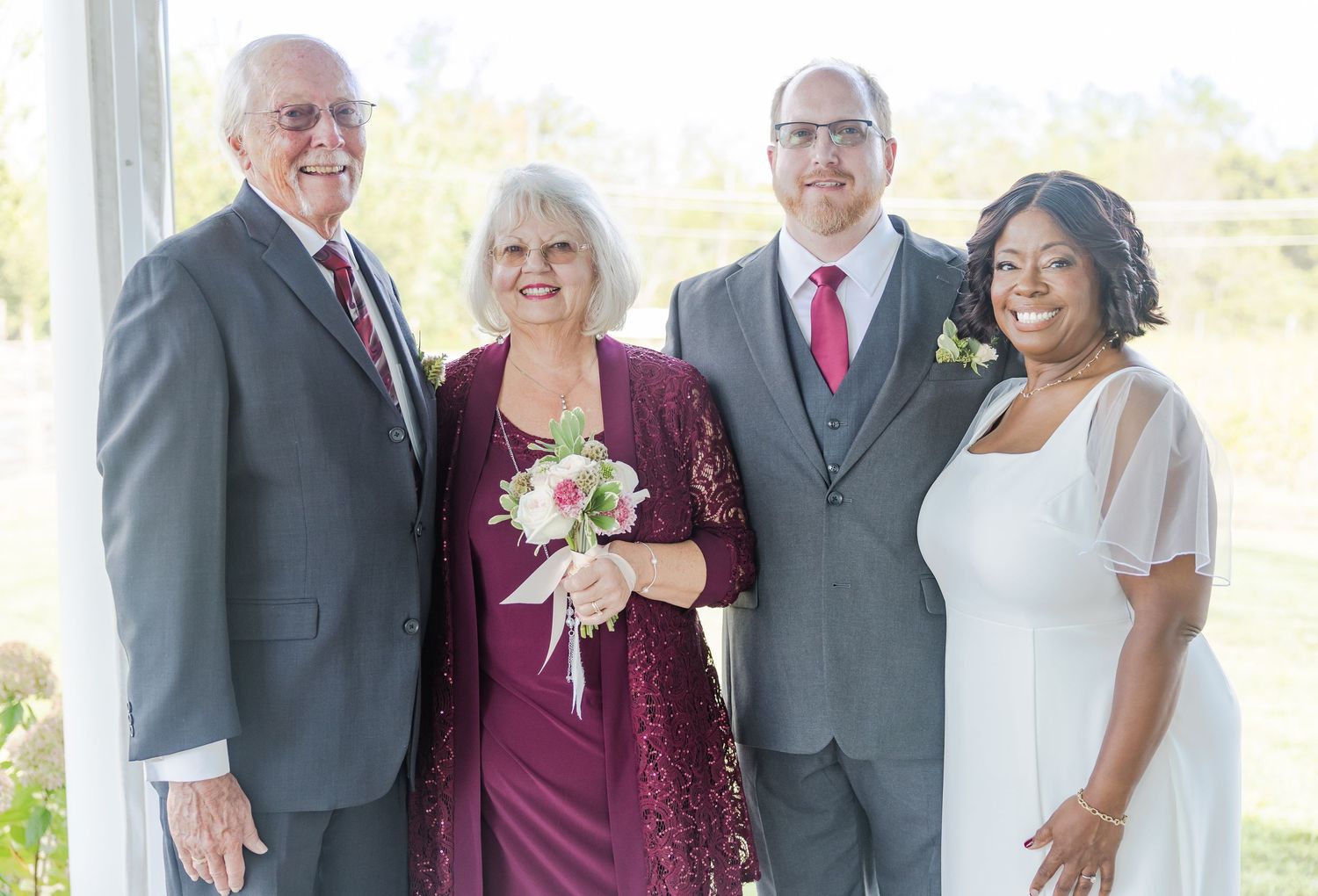 Wedding party poses together outdoors with burgundy and gray formal attire.