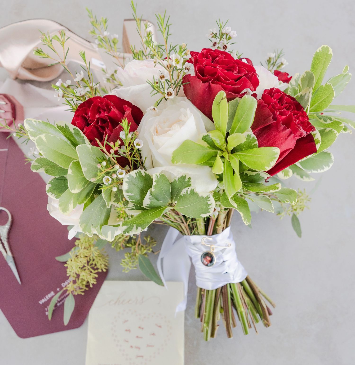 Fresh floral arrangement with red roses, white blooms and green foliage against a grey background.