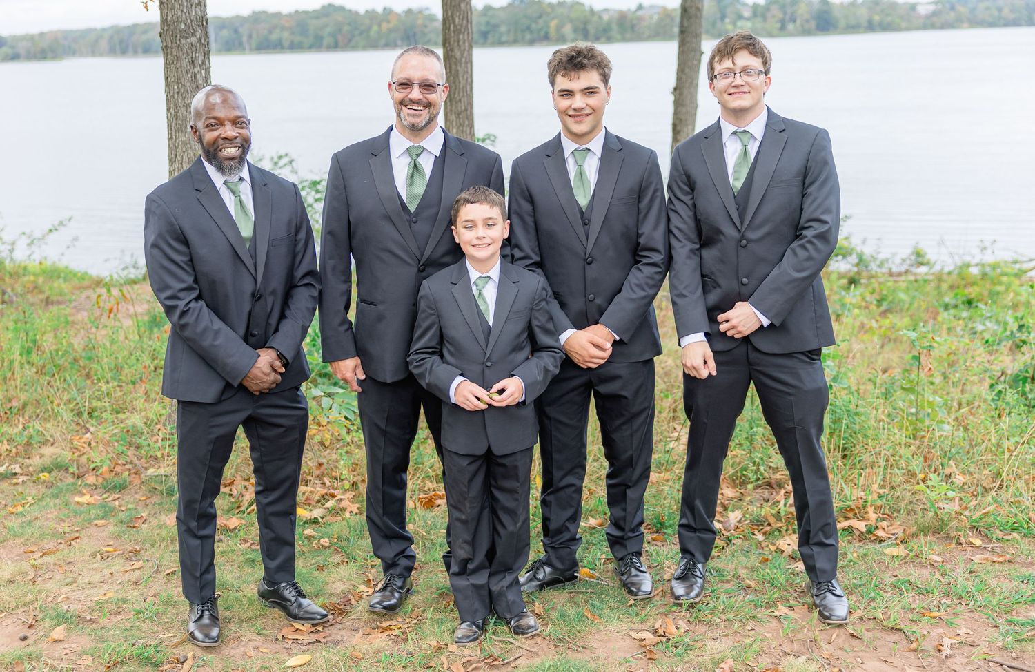 Groomsmen in dark suits pose together outdoors at wedding.