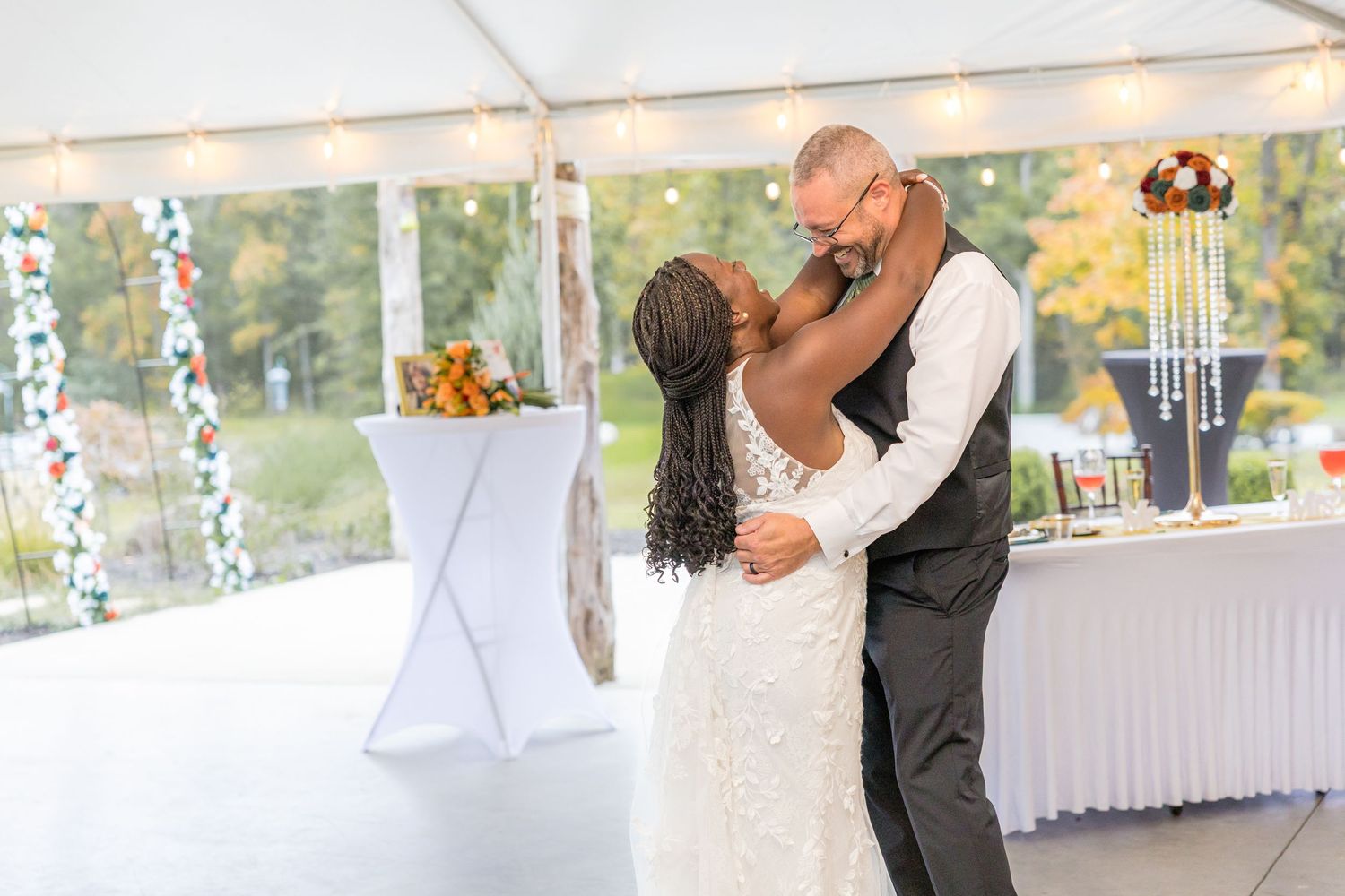 Couples dancing at a wedding reception under a white tent with string lights.