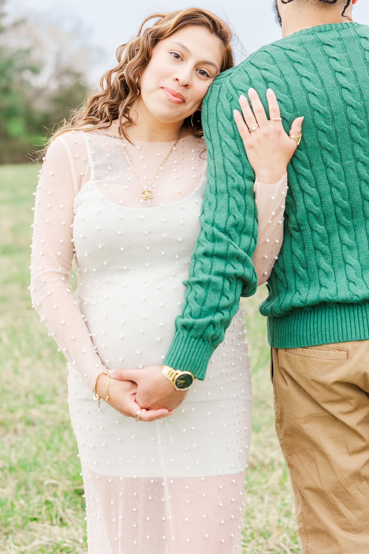 A romantic maternity photo session with a couple in white and green sweaters against a rustic backdrop.
