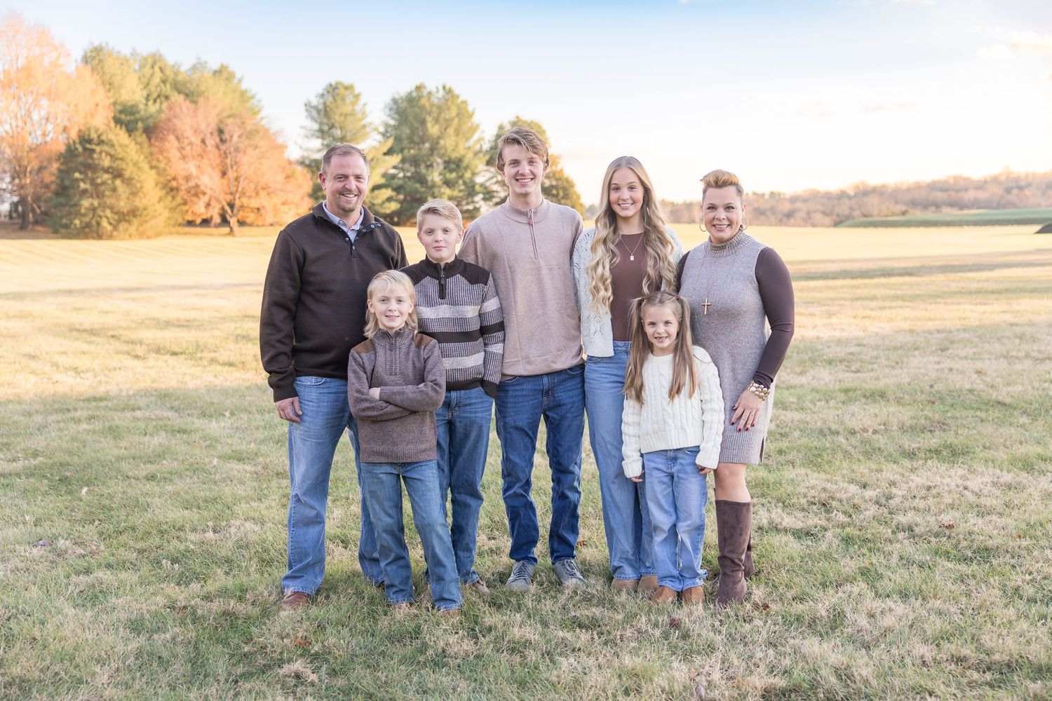 A group of people stand together outdoors in a grassy field during autumn.