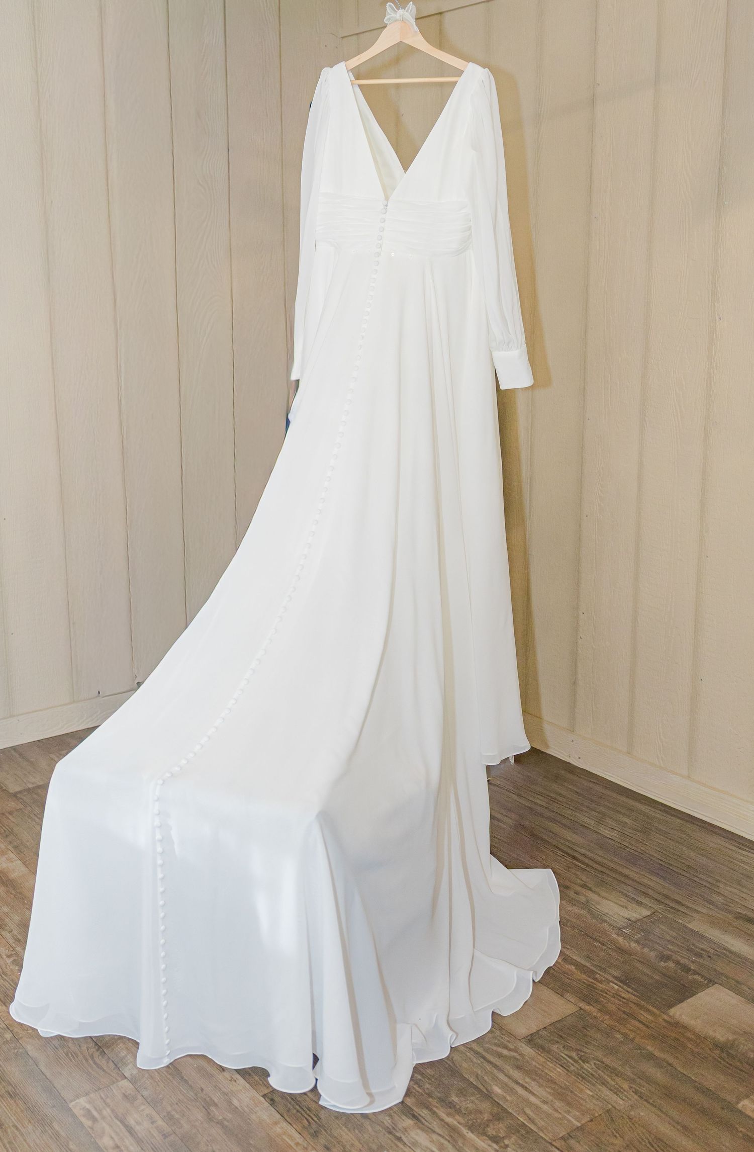 A white wedding dress hanging on display showing its elegant flowing skirt and train.