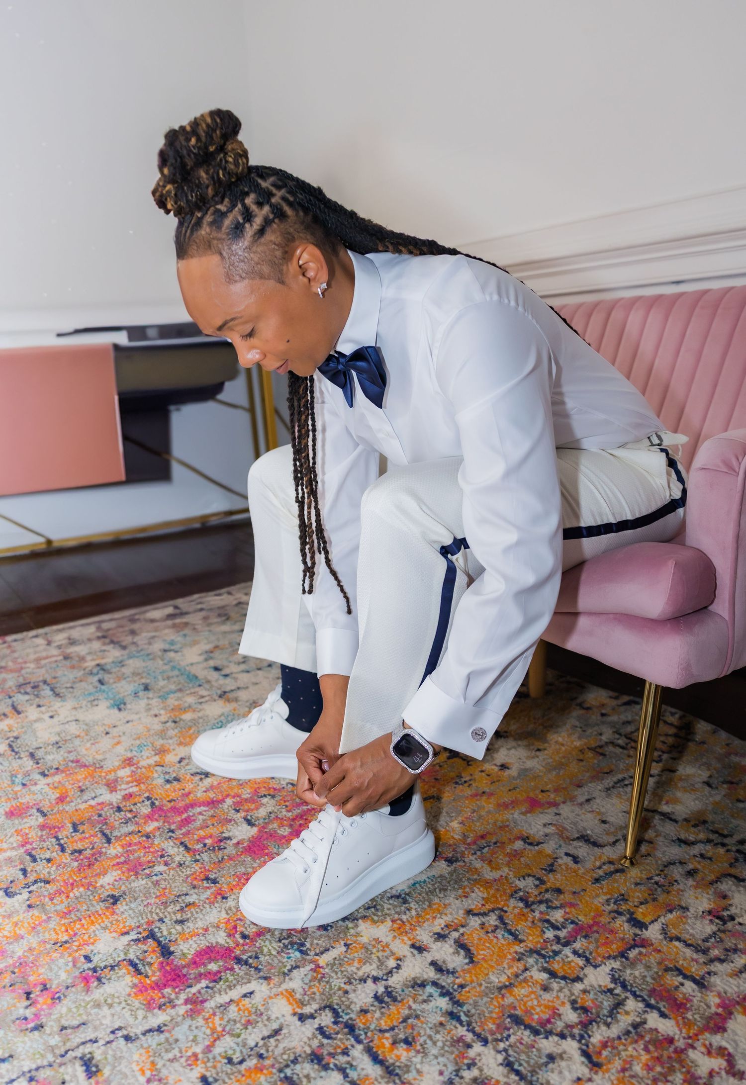 Person in white suit and navy vest crouching on a colorful patterned carpet.