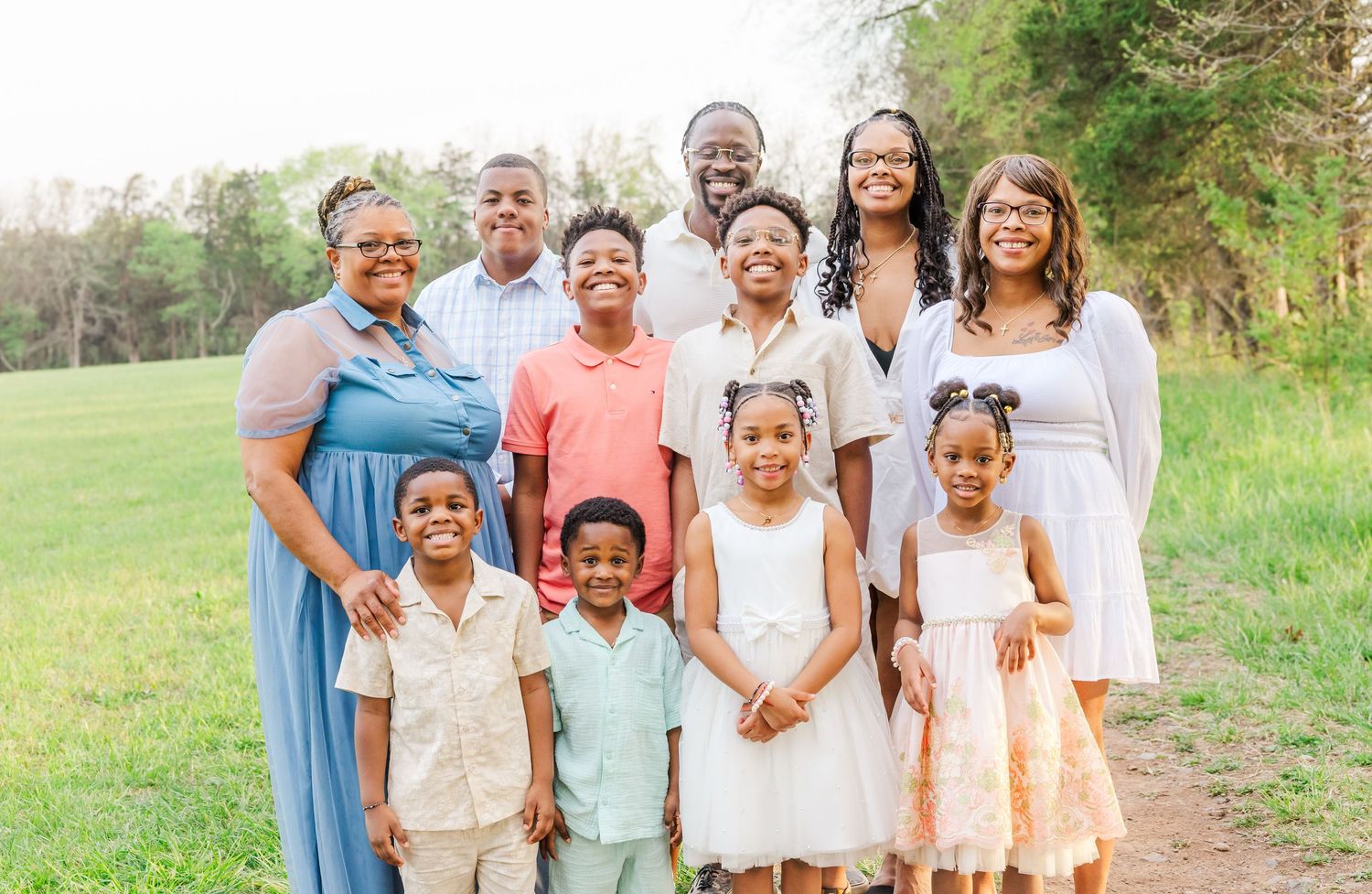 Extended family members pose together for a portrait outdoors wearing coordinated white and pastel outfits.