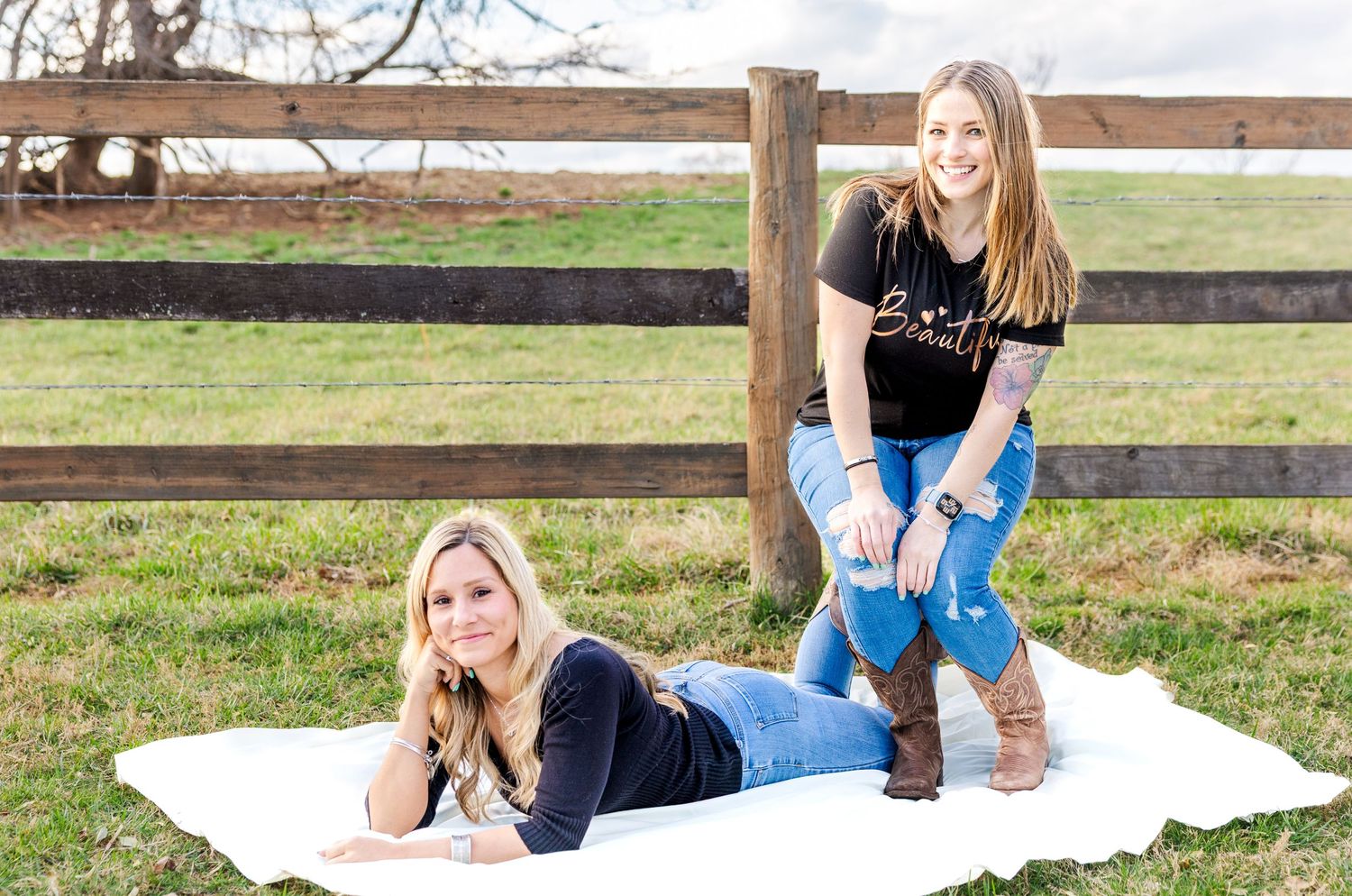 Friends posing casually on white blanket with rustic wooden fence in background.