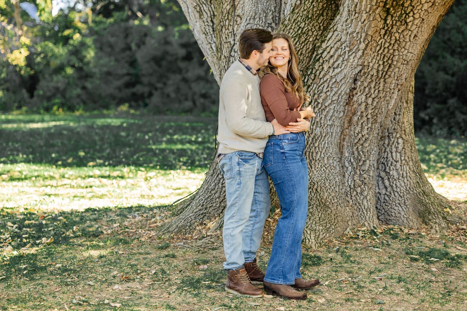 Romantic couple posing against large tree trunk in autumn park setting.