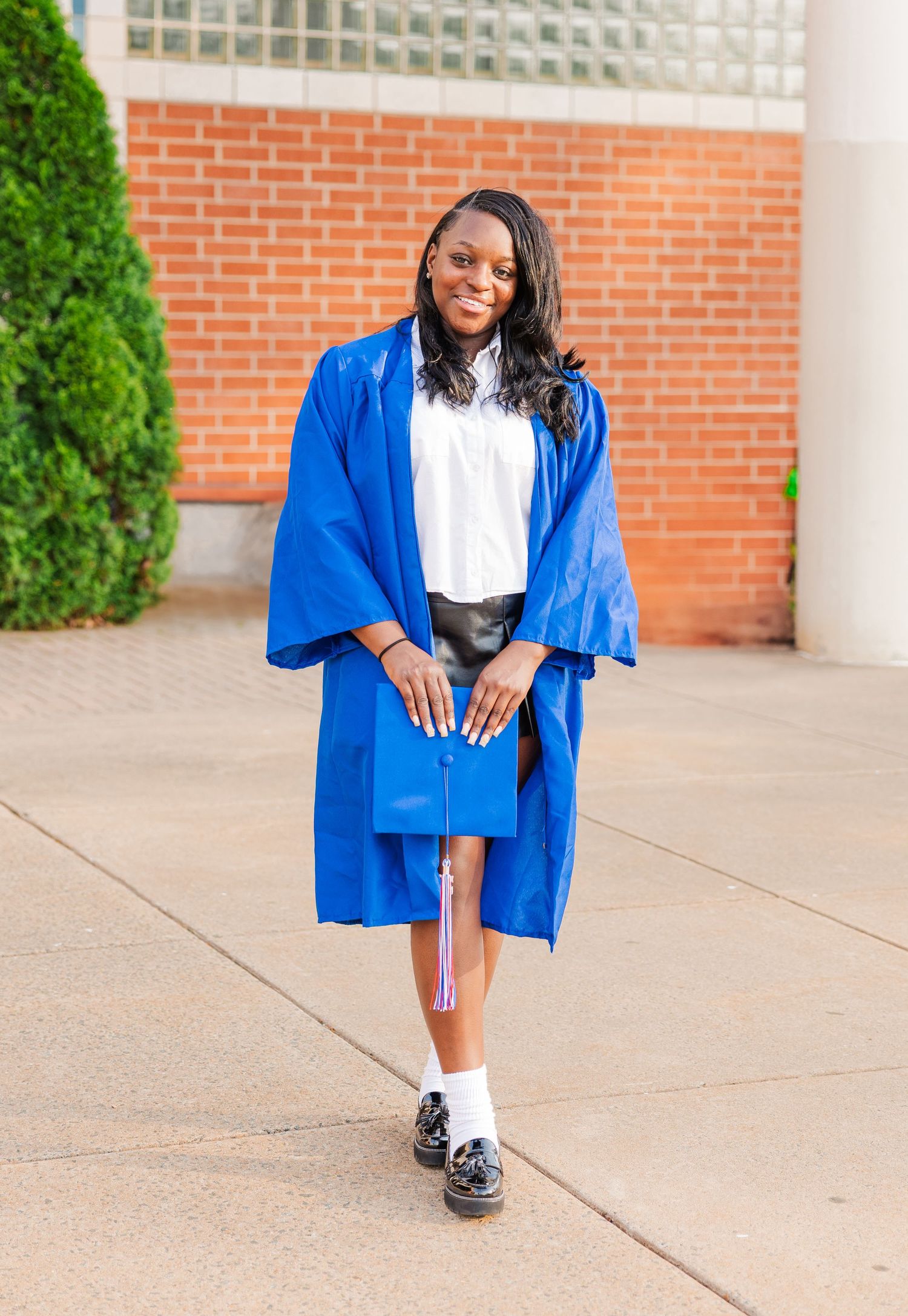 A person in a bright blue graduation gown poses on concrete near a brick building.