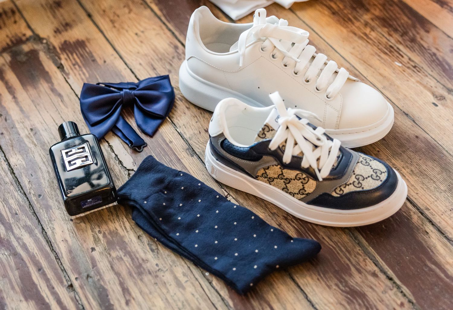 Collection of formal shoes and accessories laid out on wooden floor in preparation for wedding.