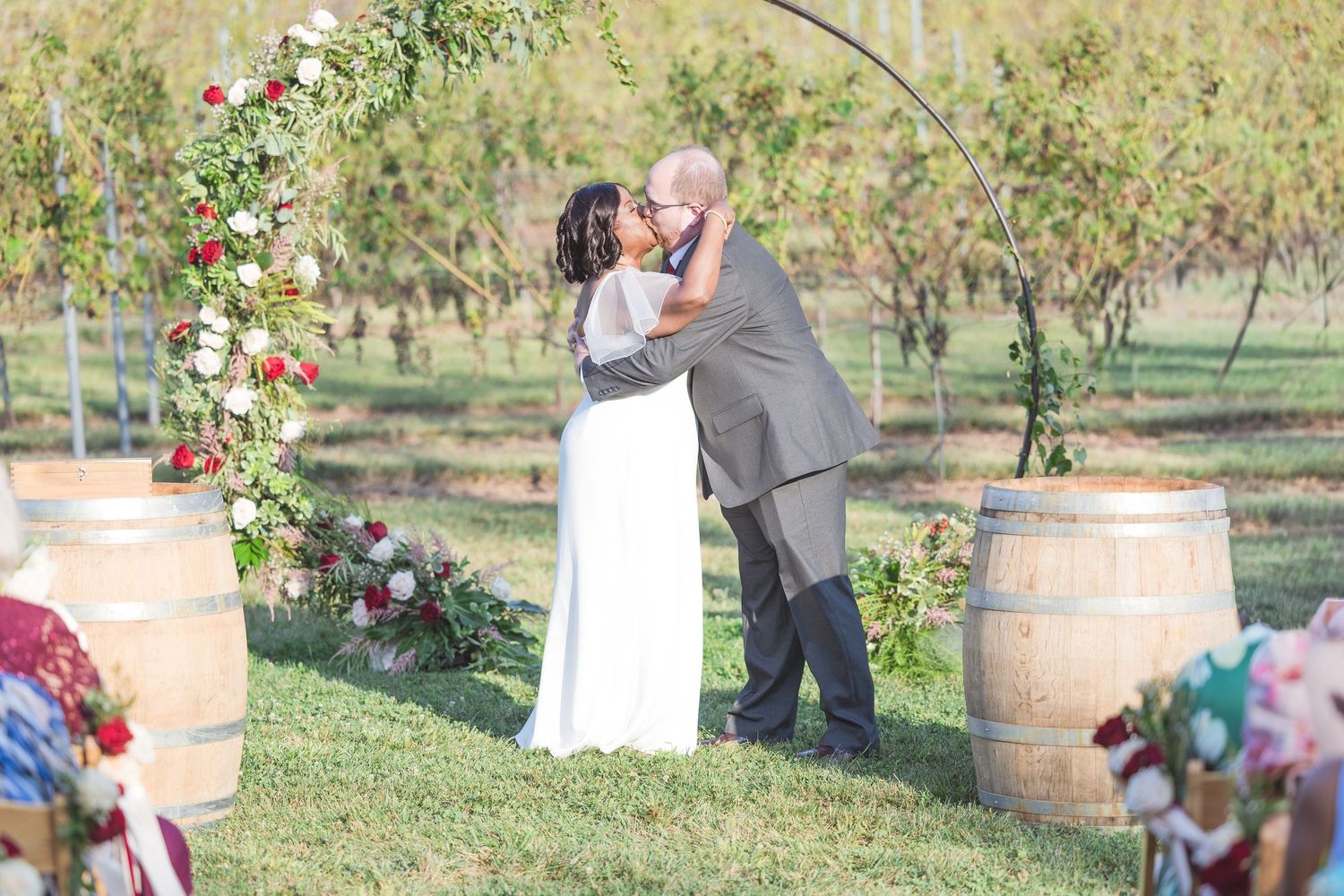 Wedding ceremony in a rustic vineyard setting with wooden barrels and natural greenery.