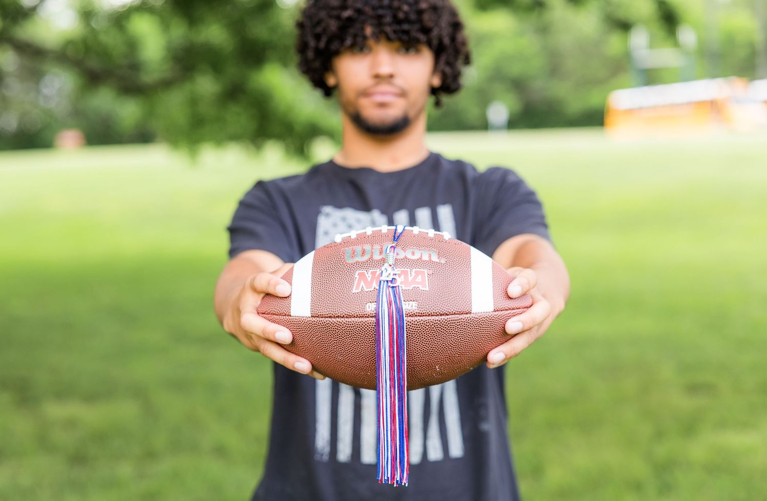 Person holds a football with purple ribbons attached while standing outdoors.