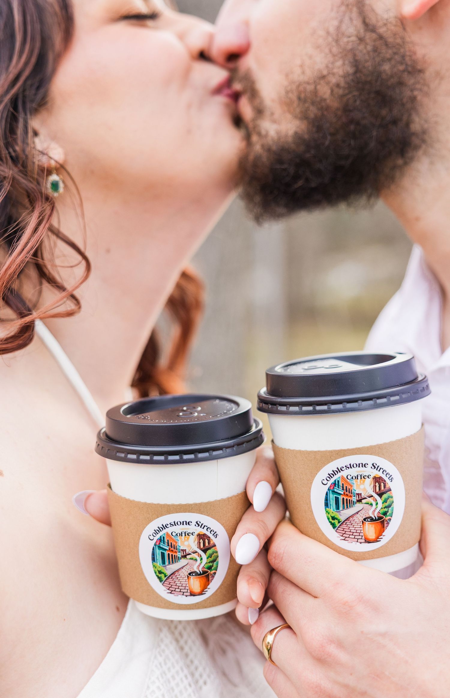 Two people share a romantic moment while holding coffee cups with a logo against a light background.