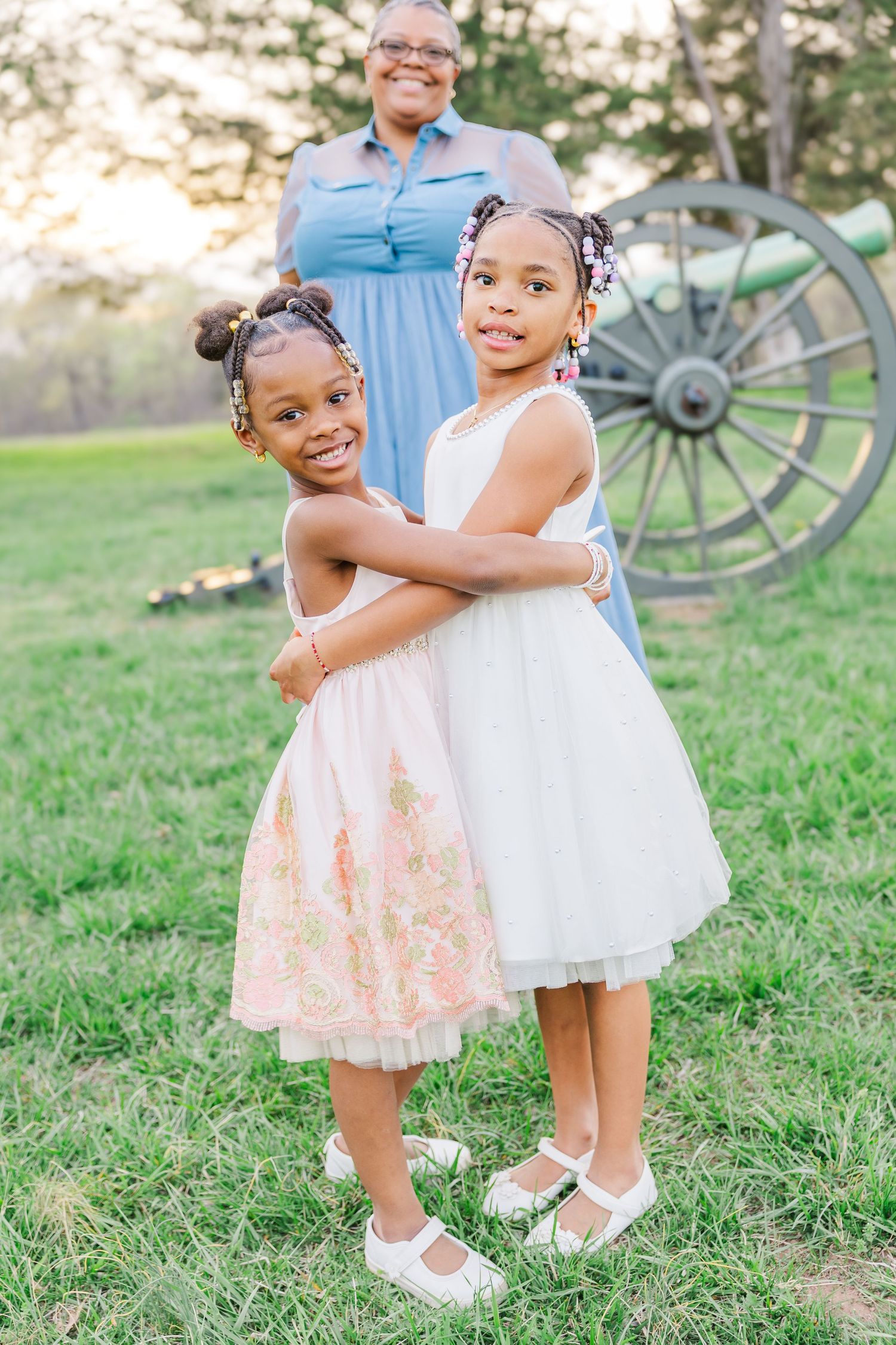 Three people pose together near an antique wagon wheel in a grassy field at sunset.