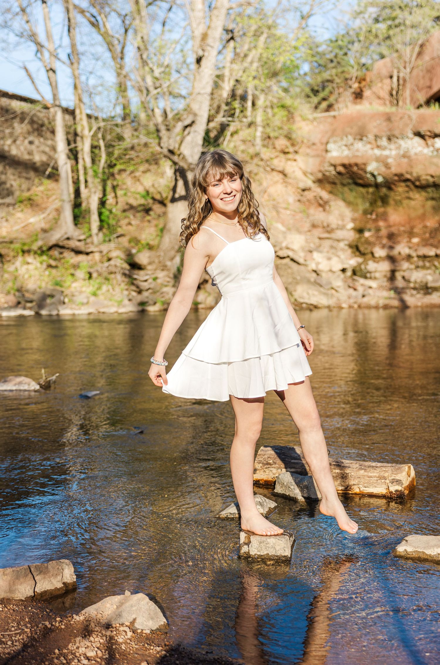 White dress and bare feet stepping on rocks in a scenic creek.