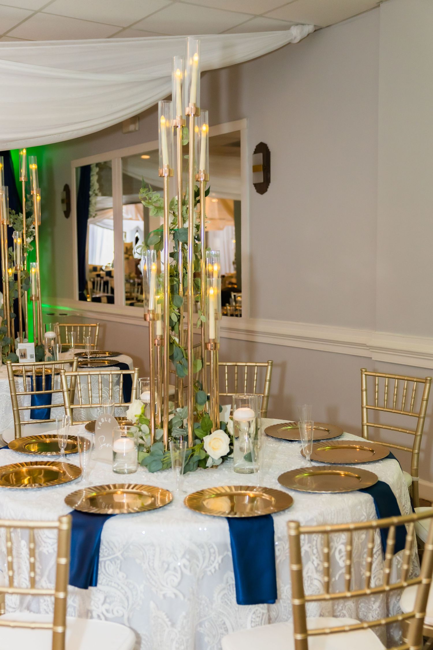 Elegant wedding reception tables set with gold chargers, navy linens, and white tablecloths.