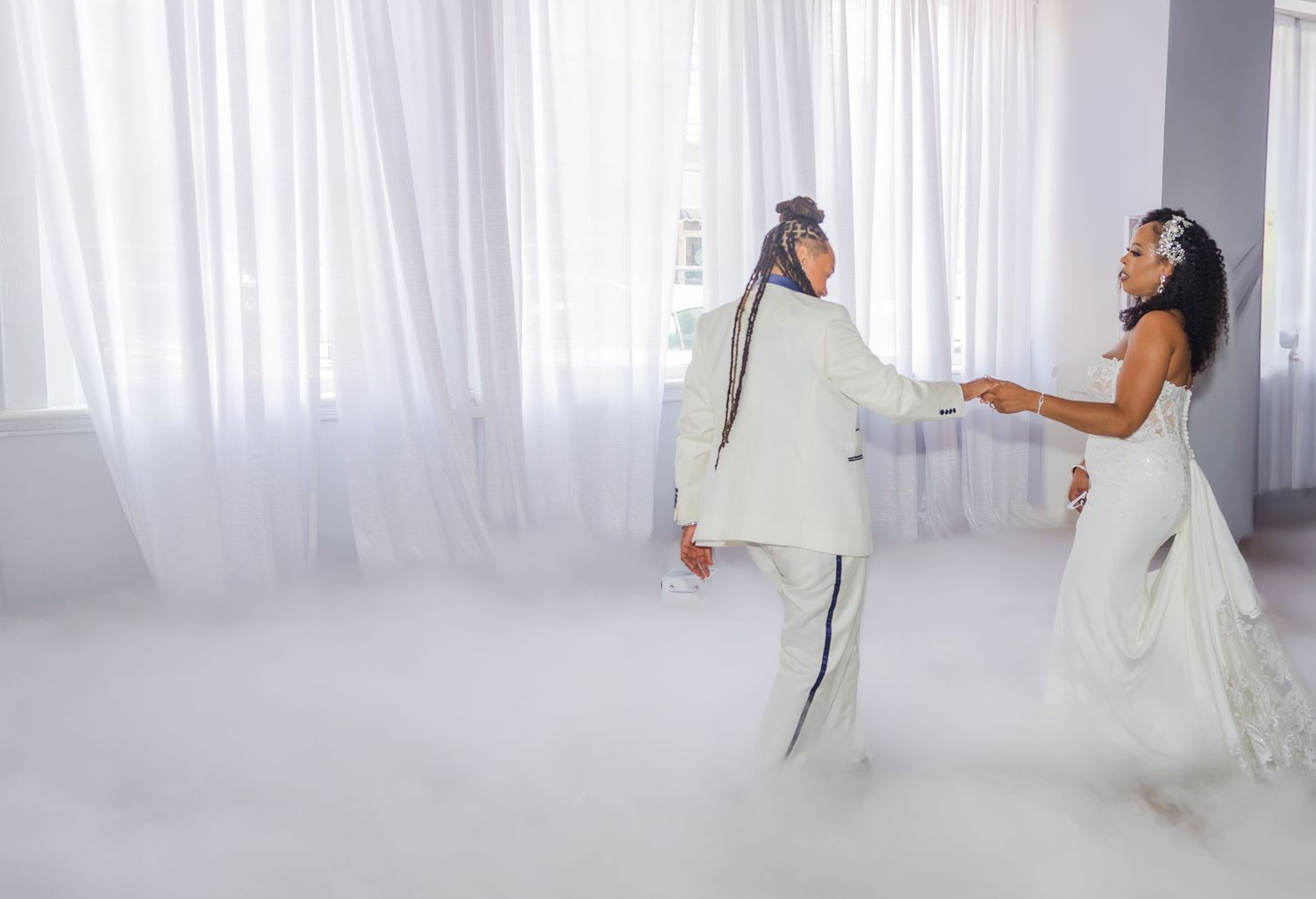 A couple dances in an ethereal setting with white curtains and fog effects.