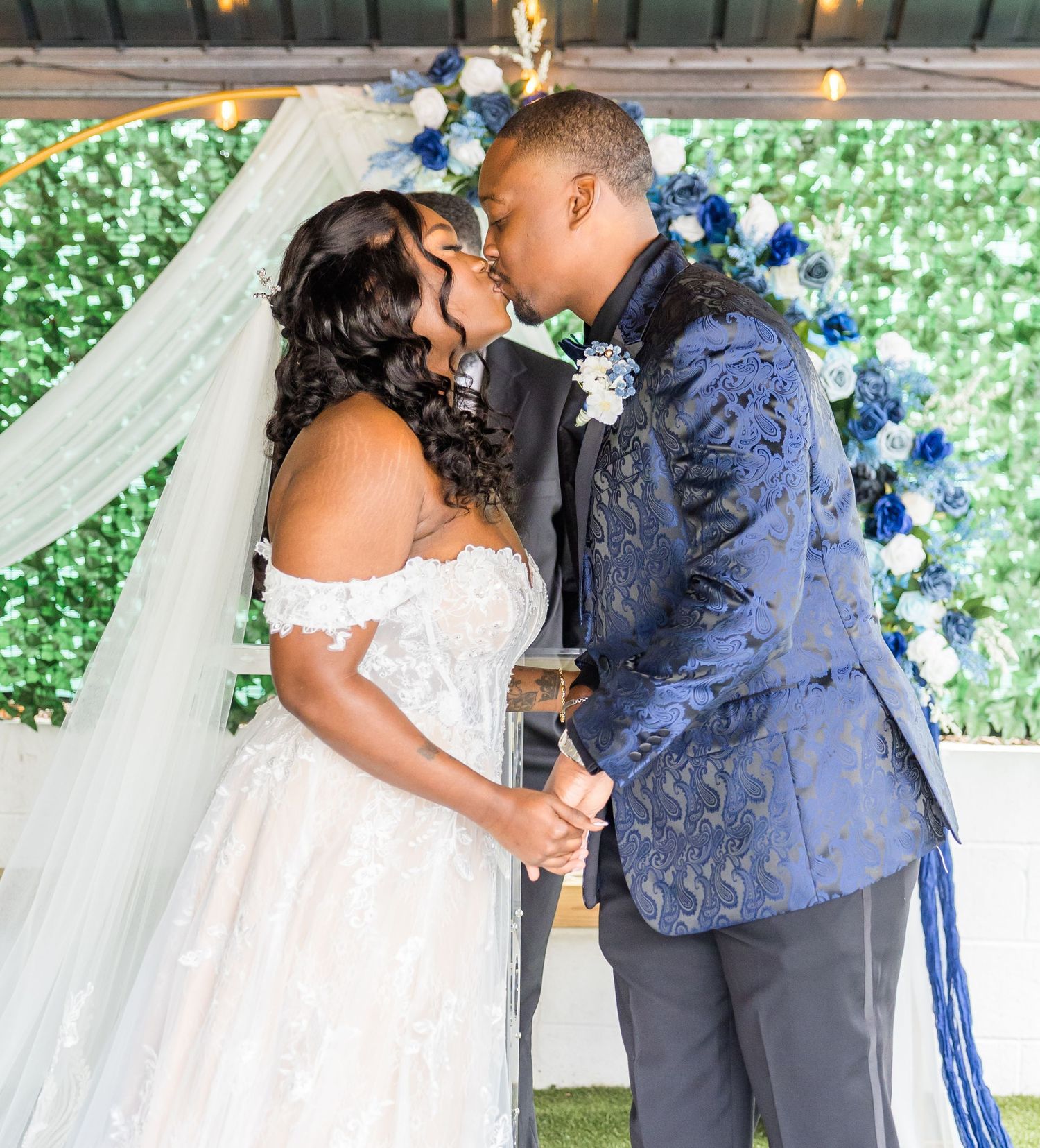 A couple shares a romantic moment during their wedding ceremony with a floral backdrop and elegant decor.