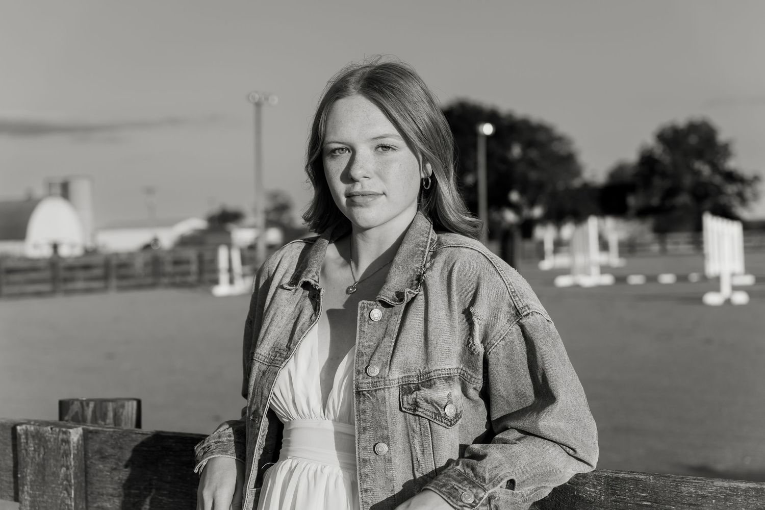 Young woman in denim jacket poses outdoors at a farm in a black and white portrait photo.