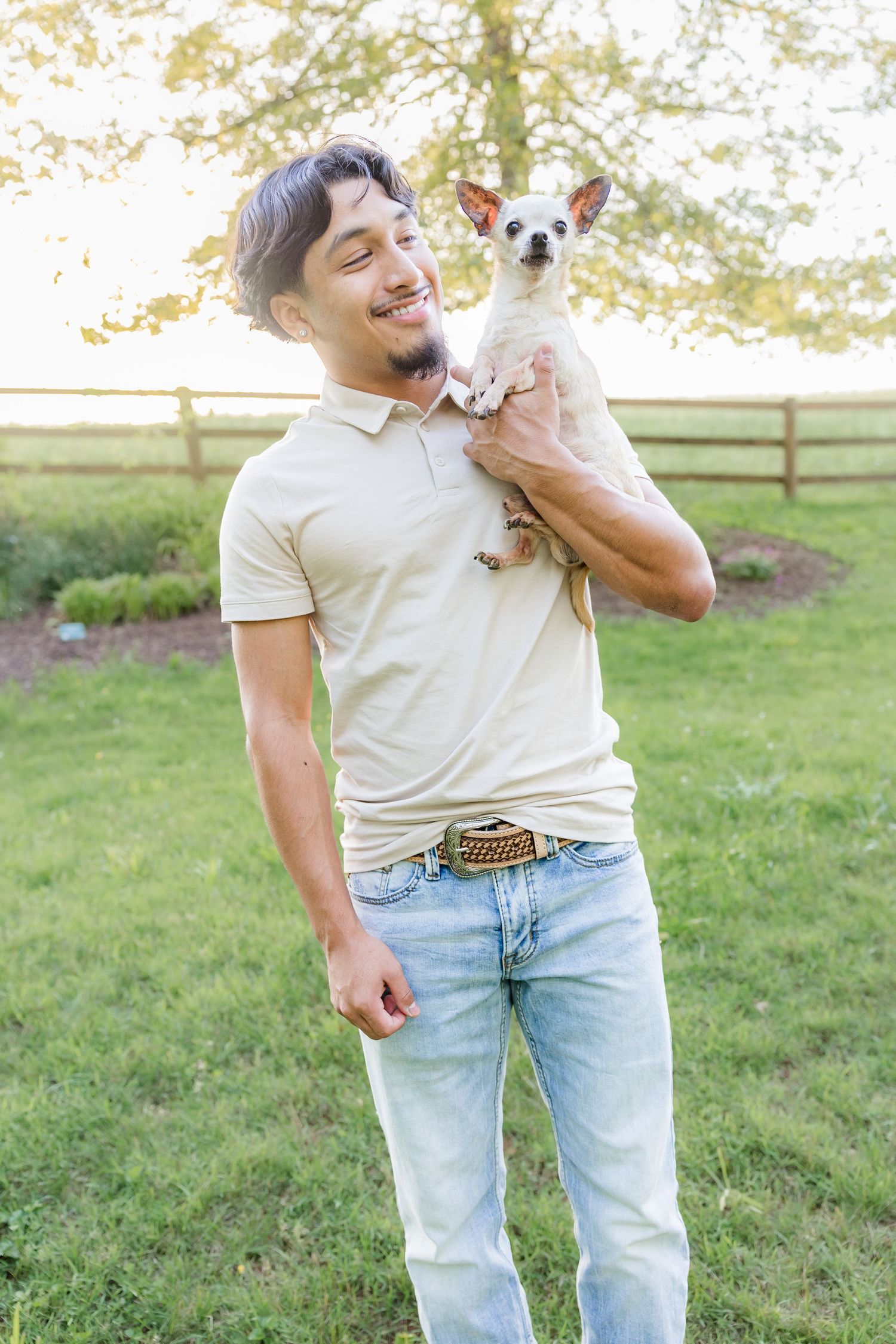 Person in light jeans and white shirt holding a small white dog outdoors.
