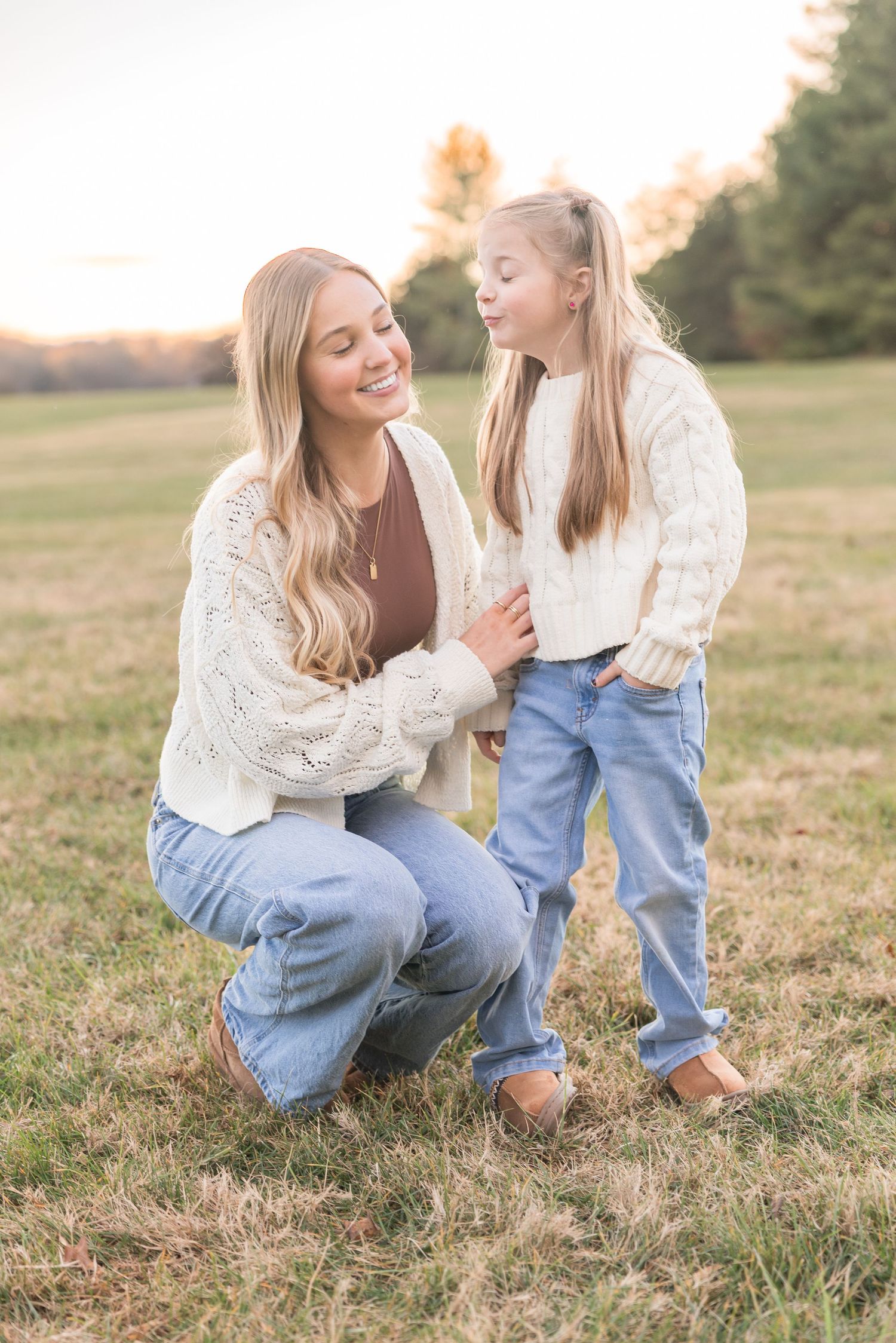 A mother and daughter share a tender moment together while sitting in a grassy field at sunset.