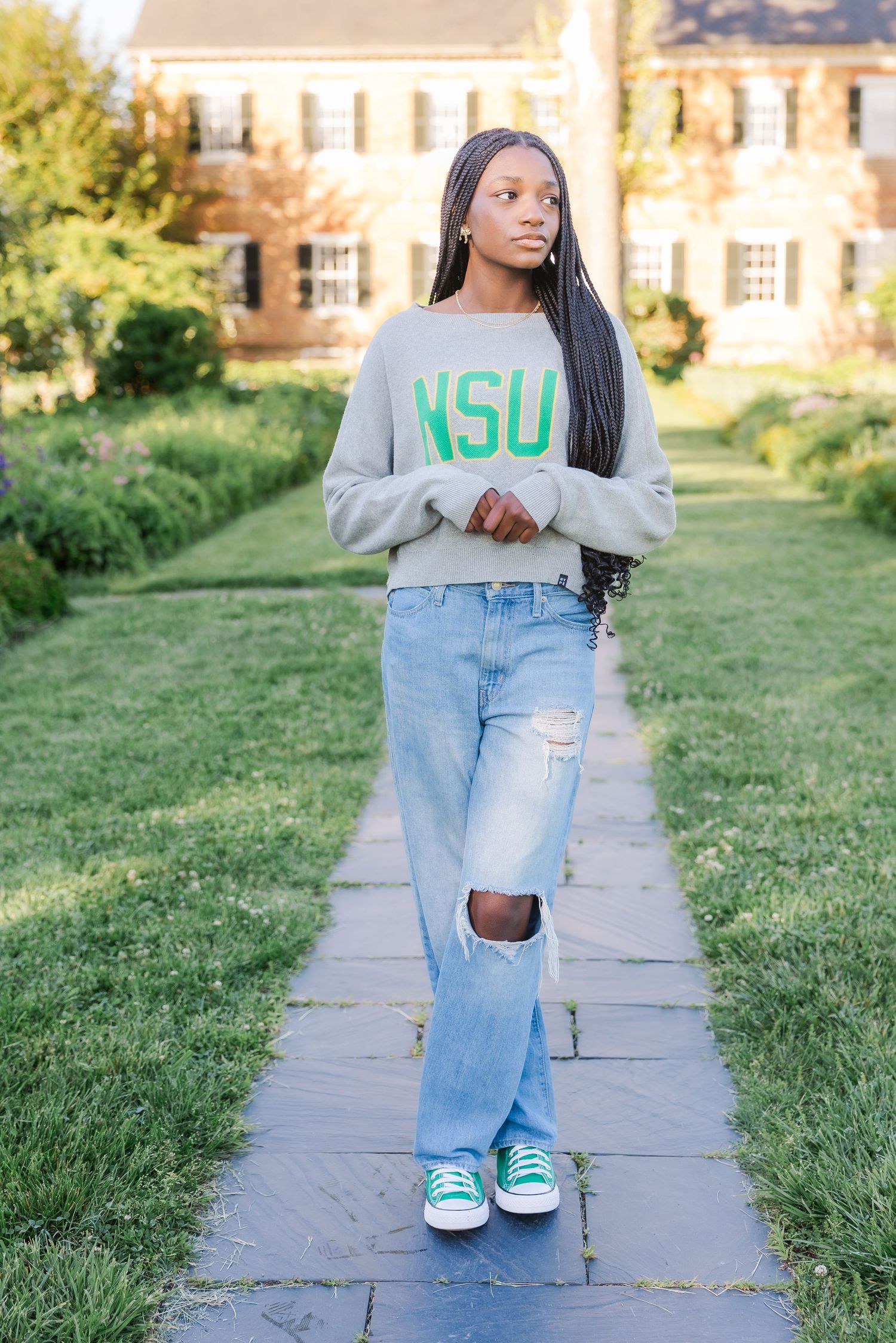 Student in gray NSU sweatshirt and ripped jeans stands on stone walkway.