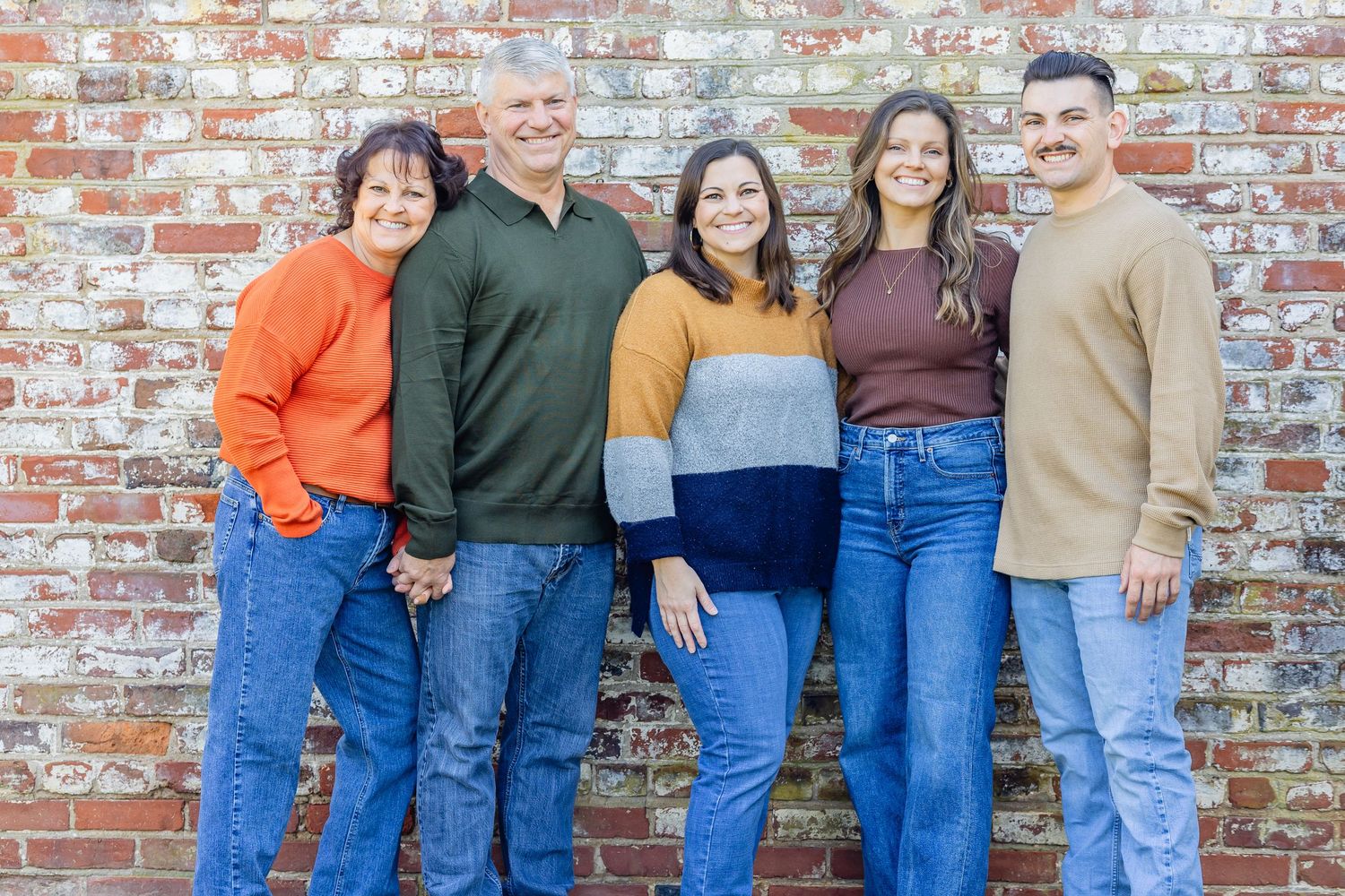 Extended family group portrait against rustic brick wall background.