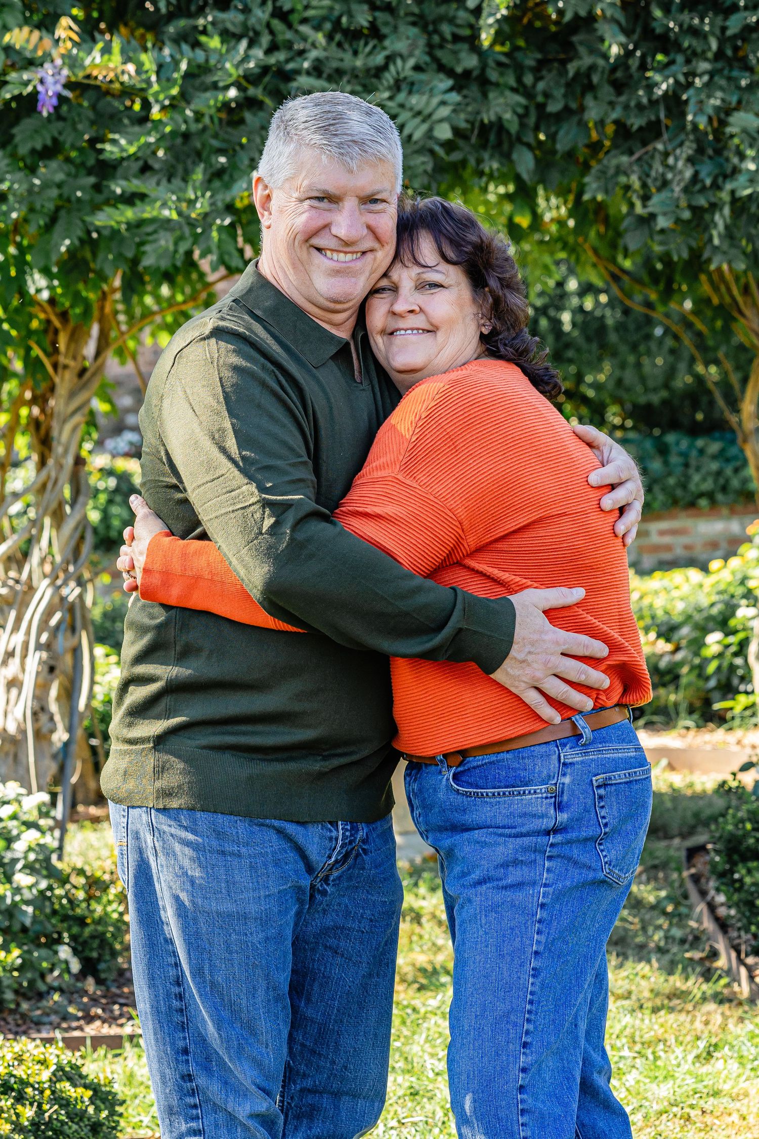 Couple in casual wear sharing warm embrace outdoors in garden setting.
