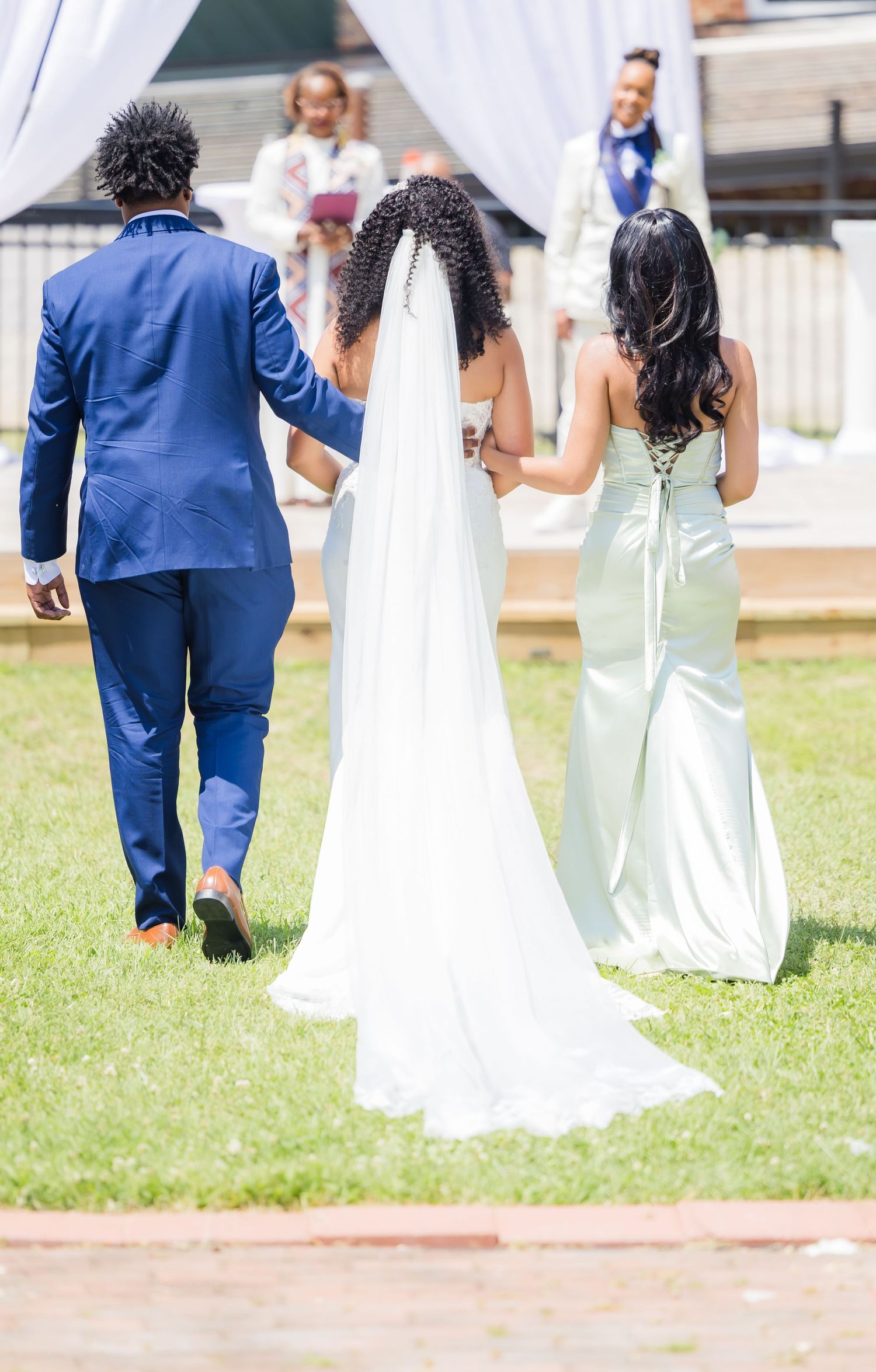 Wedding party walking on grass with bride in white gown and attendants in formal attire.