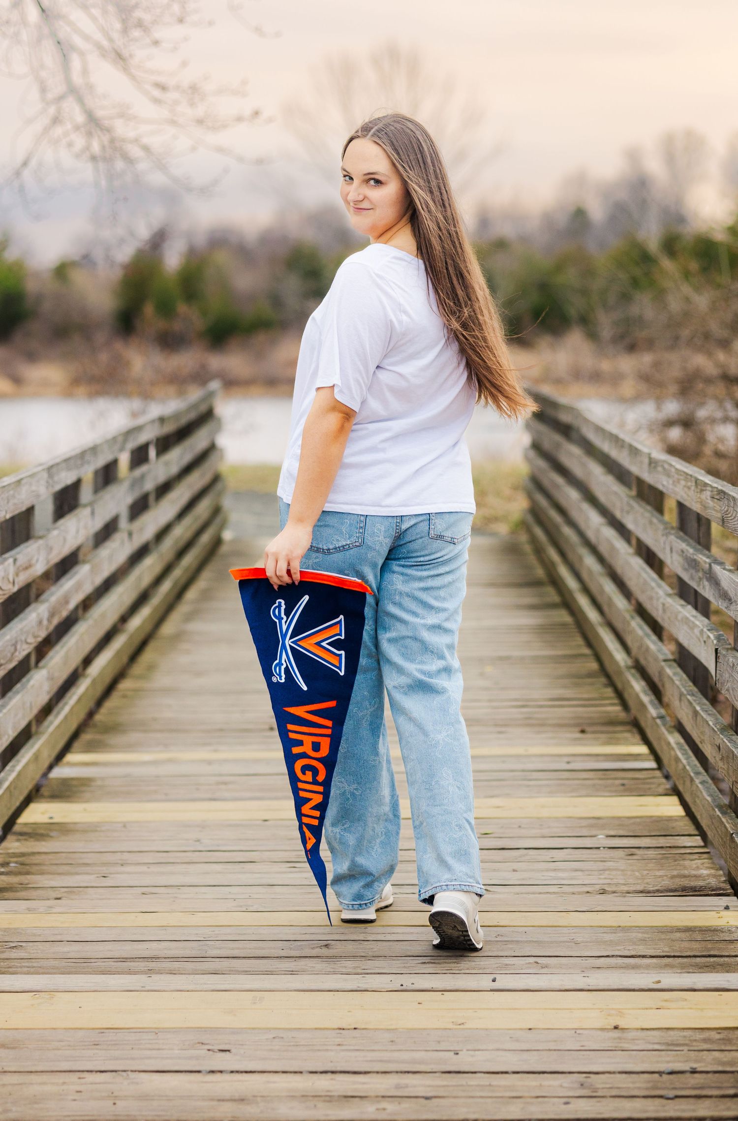 Student displaying Virginia school pride with pennant while standing on wooden boardwalk.