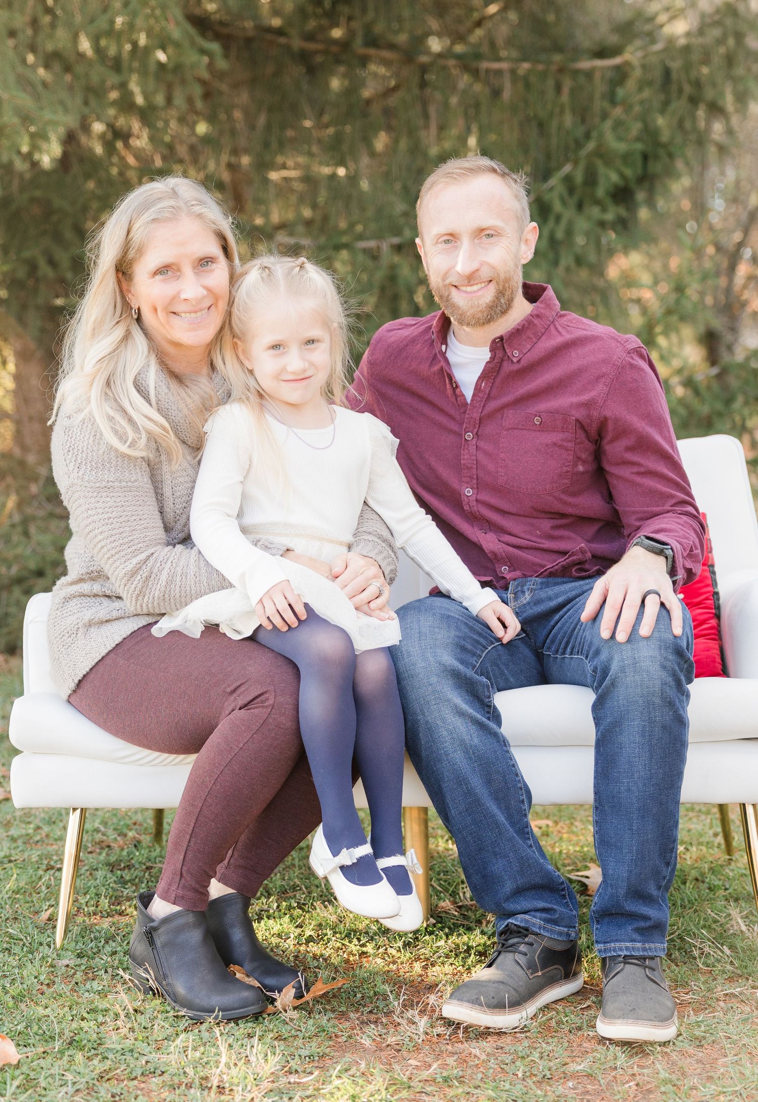 Family members sitting together on white benches outdoors in autumn with fallen leaves on the ground.