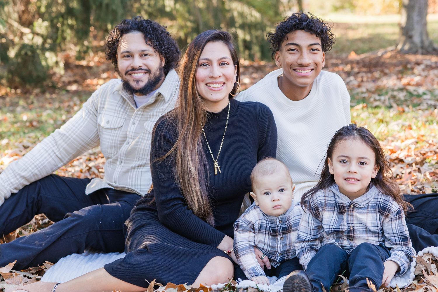 A family sits together on fallen autumn leaves during an outdoor photo session in a park.