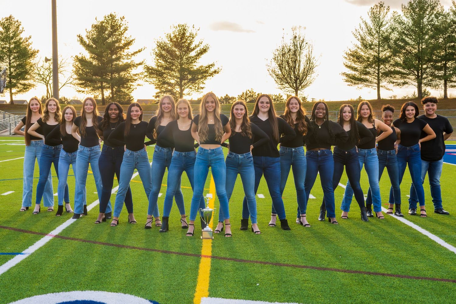 Wide group shot of cheerleading team members lined up on a football field at sunset.