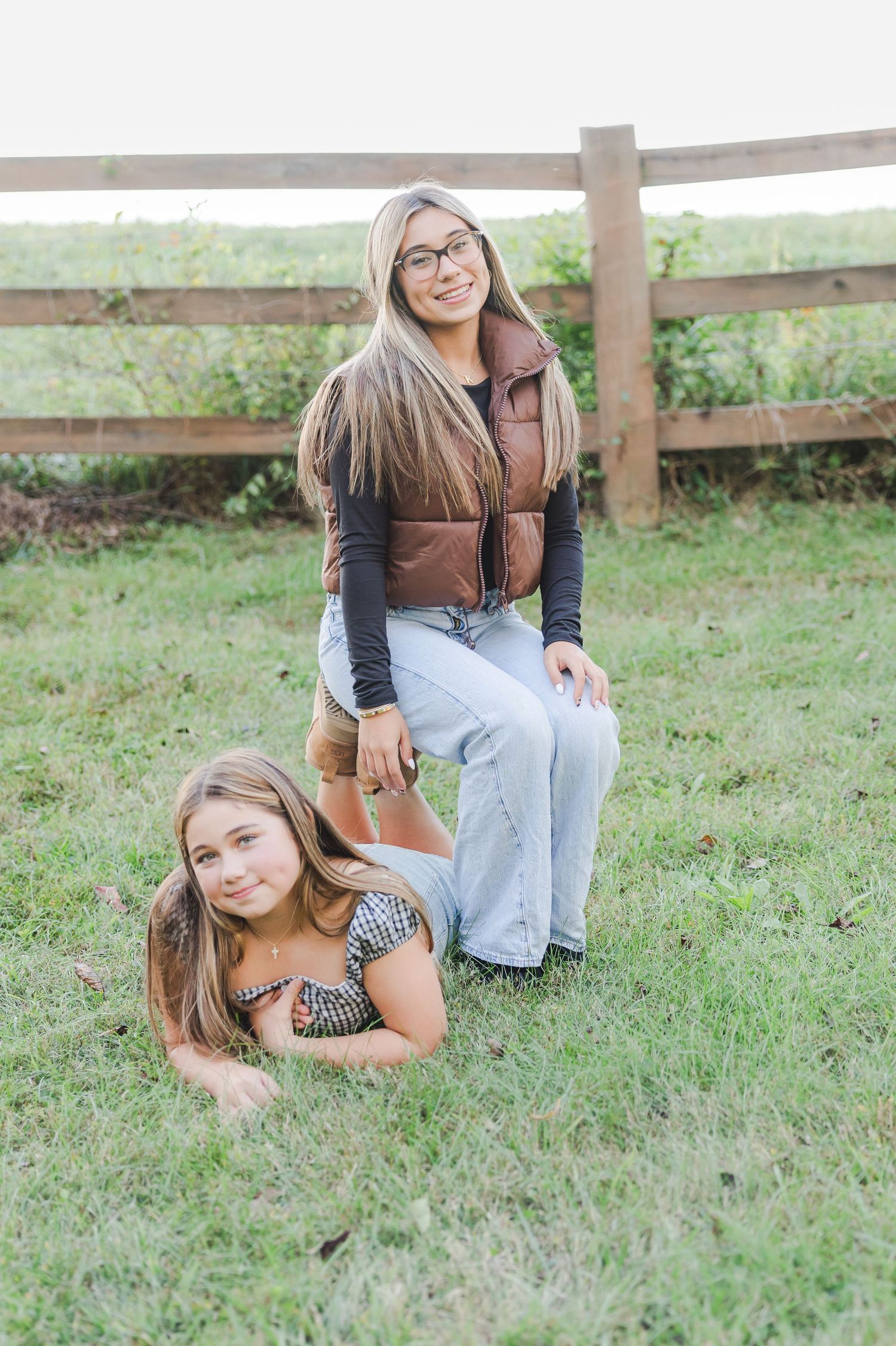 Two people sit casually on grass near a wooden fence on a sunny autumn day.