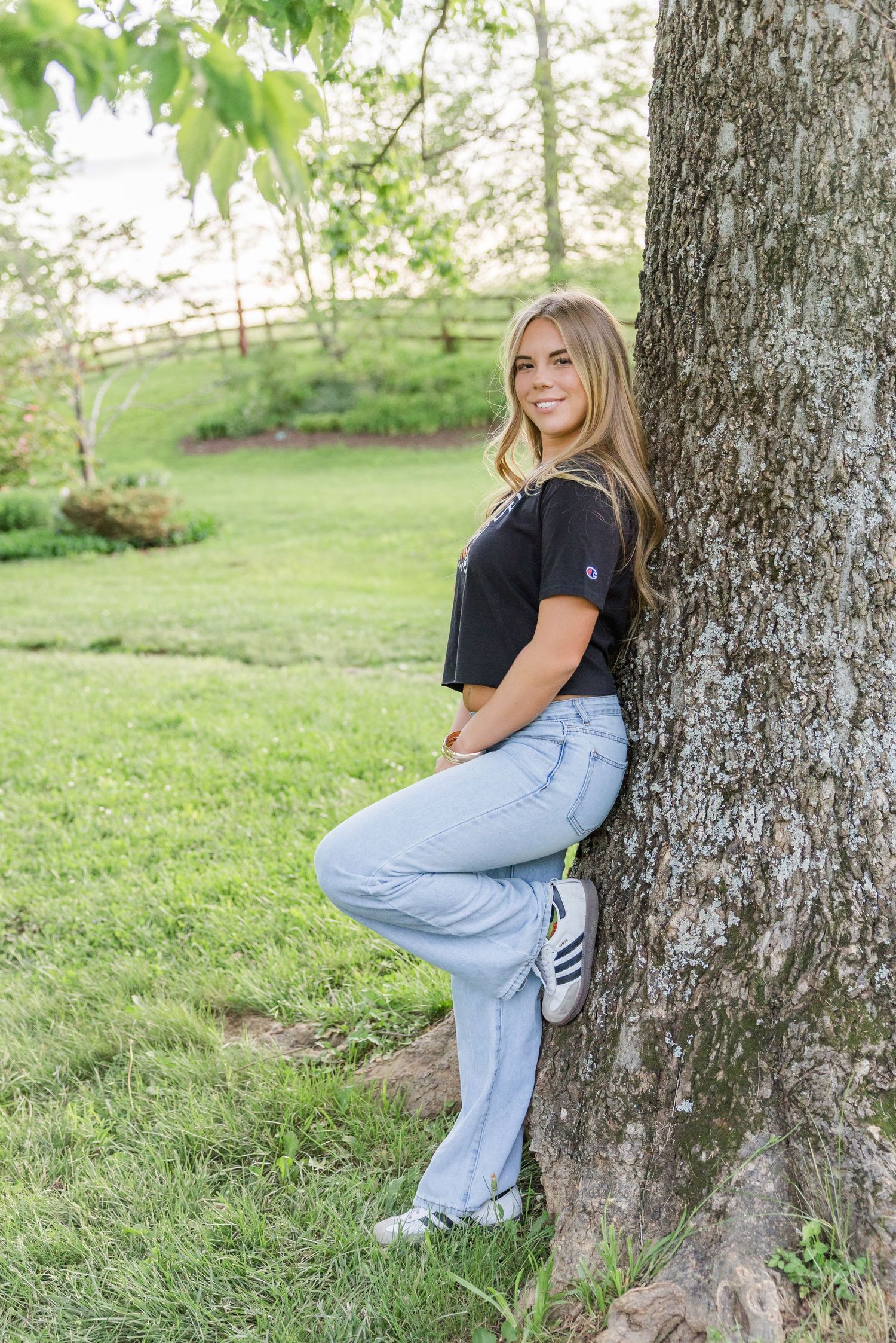Casual outdoor portrait session showing woman in denim leaning against a tree trunk.