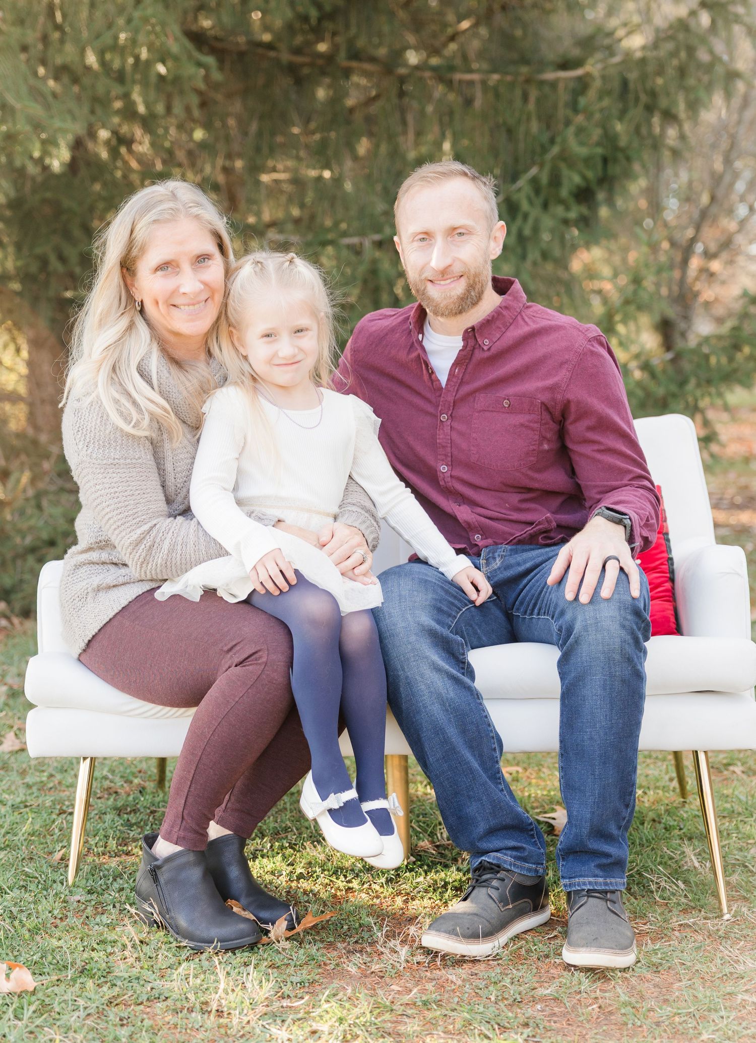 Family sitting together on white bench outdoors in casual clothing during autumn photo session.