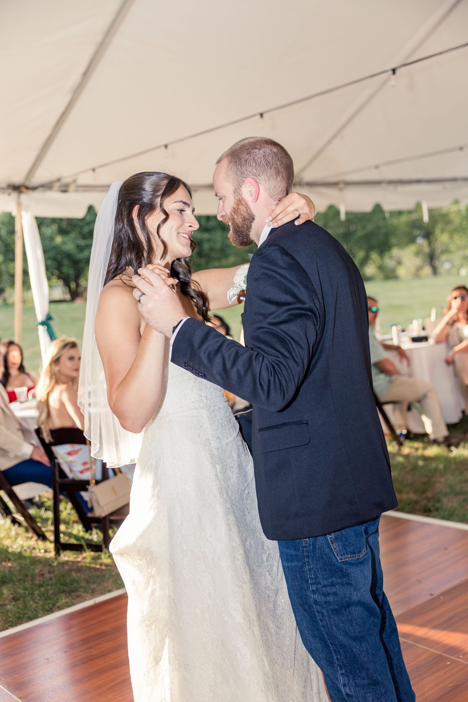 Bride and groom share their first dance under a white tent at an outdoor wedding reception.