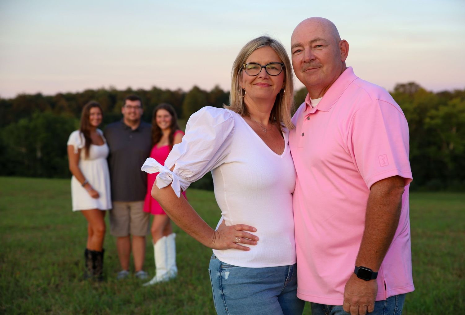 Family group wearing pink and white outfits posing together outdoors at sunset.