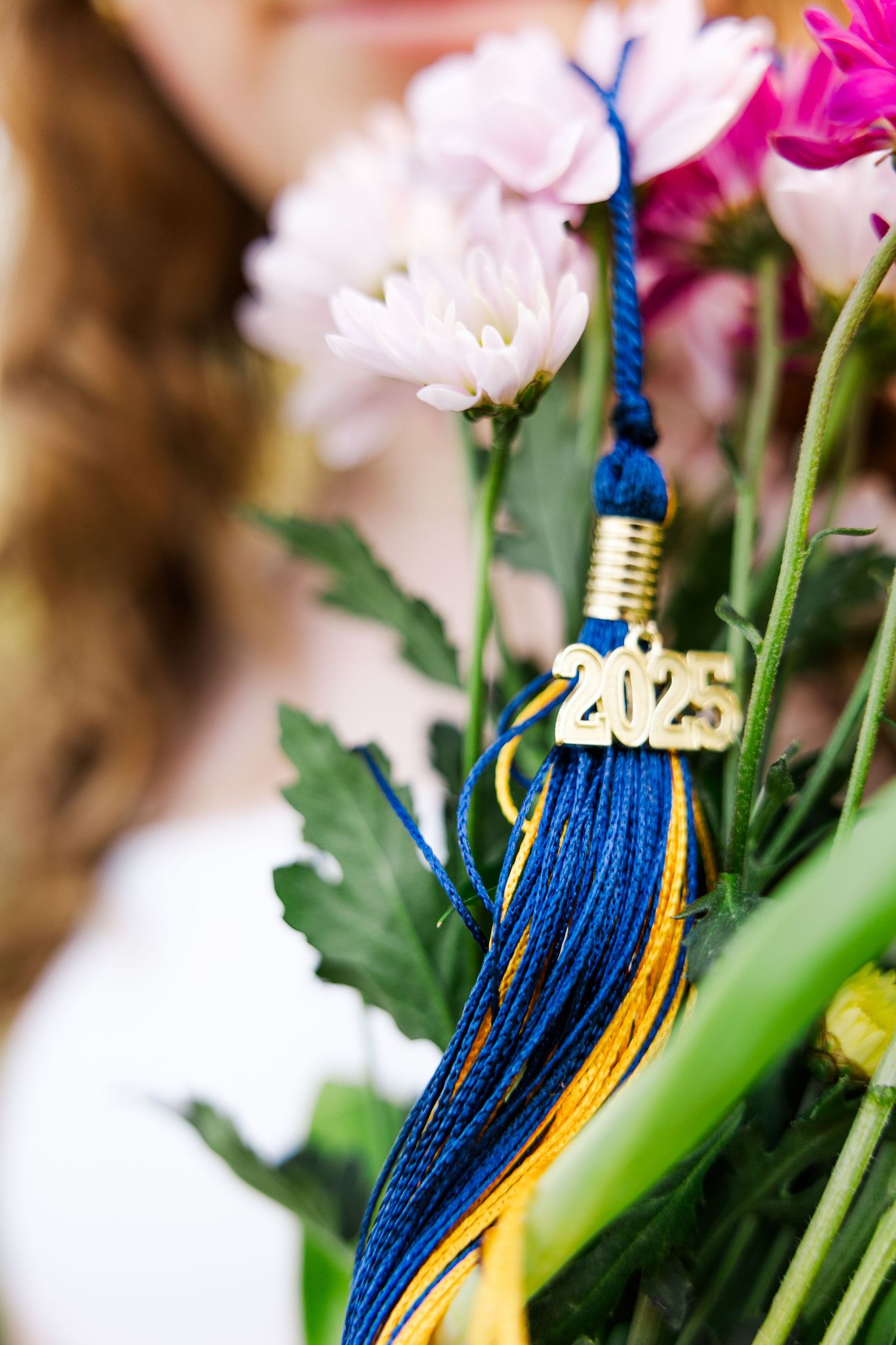 Graduation tassel in blue and gold with 2023 charm among pink flowers.