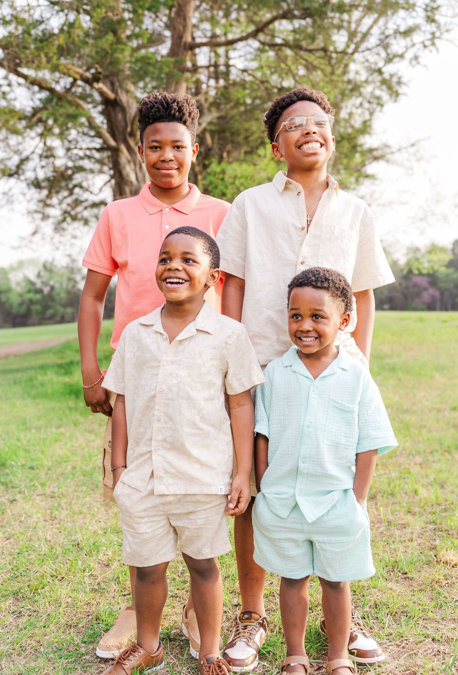 Four siblings stand together outdoors wearing coordinated casual outfits in pastel colors.