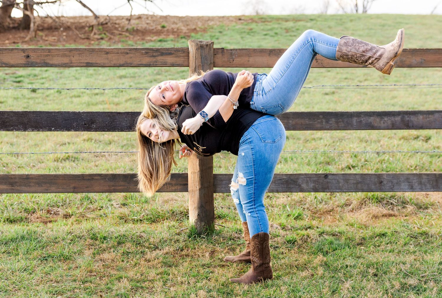 Two friends having fun posing playfully against a wooden fence in a field.